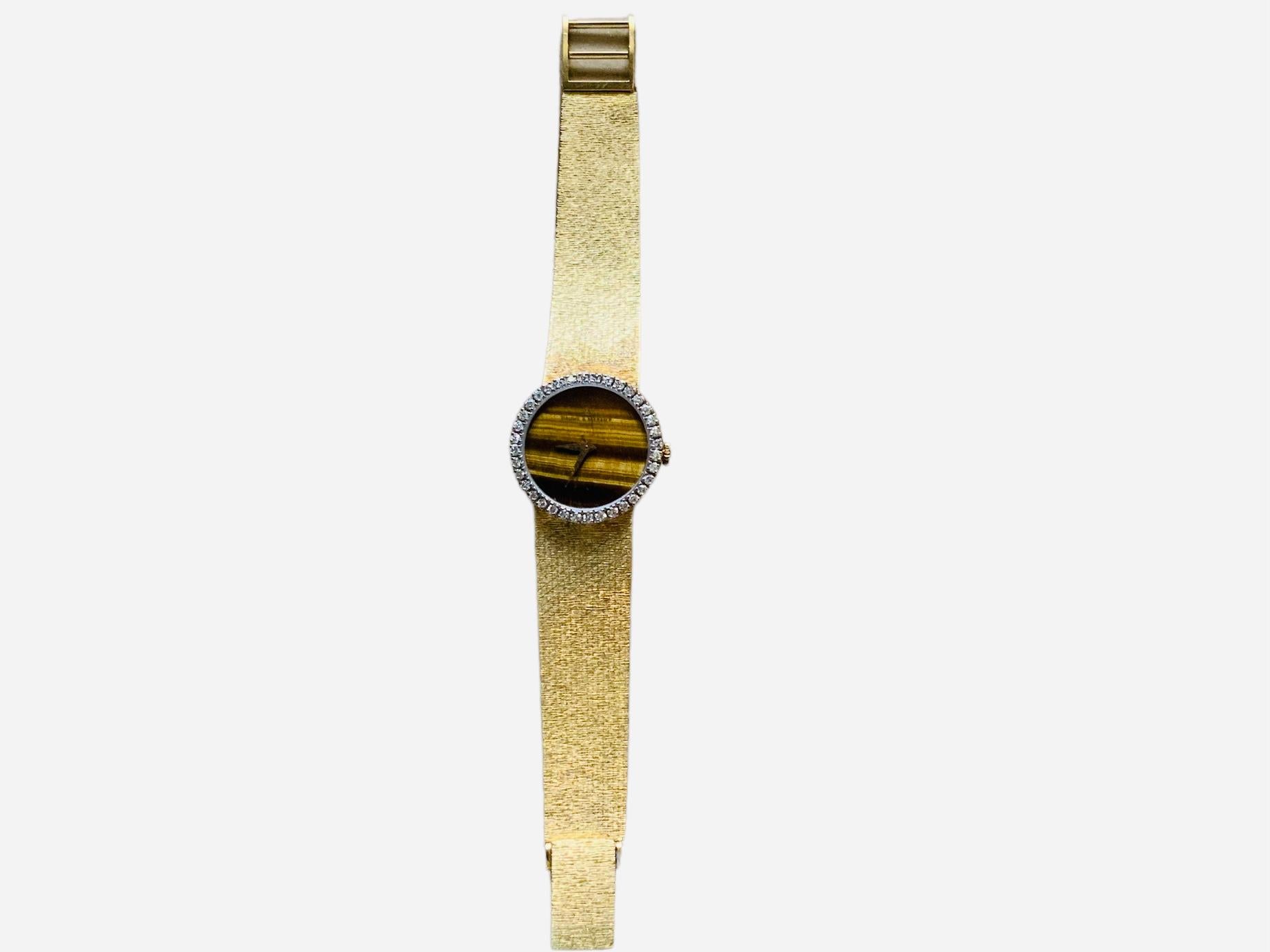 This is a 18K gold Lady’s Baumé & Mercier Watch. It is recognized as an elegant dress watch. It has a manual winding movement. The round dial is made of Tiger Eye and is hallmarked Baume & Mercier , Geneve at the top . It has gold tone minute