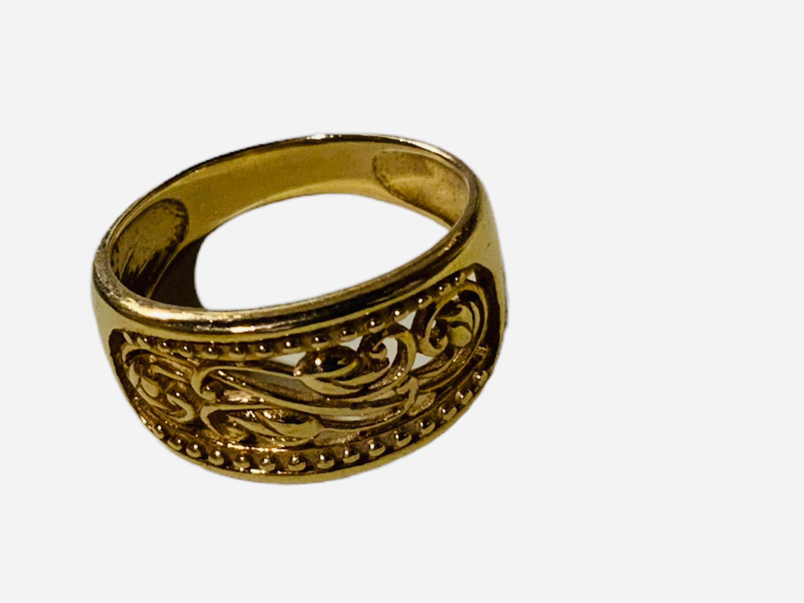 This is an 18K gold ring made in Turkey. It depicts a wide band with a pierced longitudinal center that is adorned with few scrolls of floral branches and some beads in line framed them. The ring is hallmarked AK, Turkey and 18K.