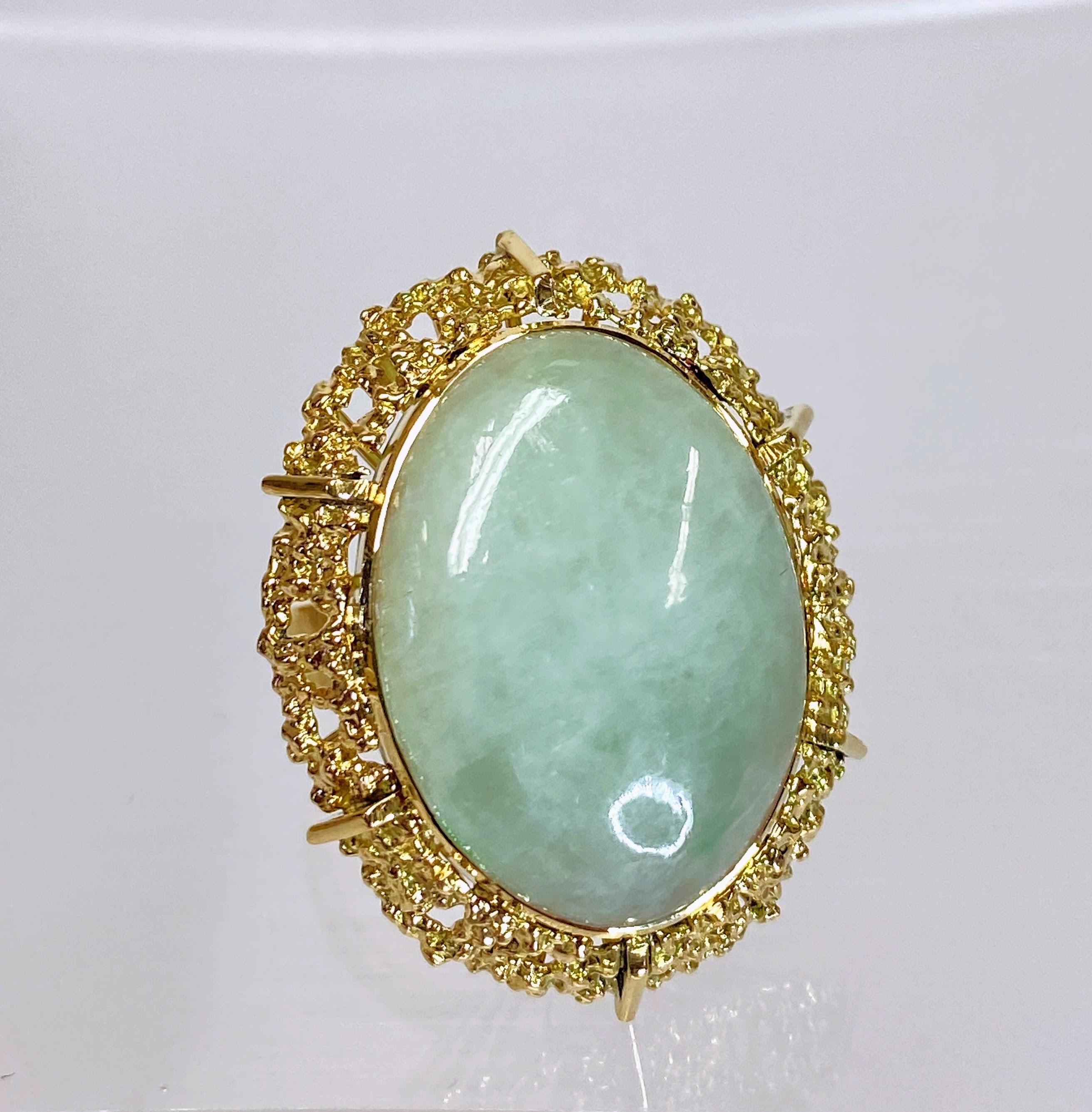 This vintage 18K yellow gold Mid-Century 1960s oval cut grand jade ring is a remarkable blend of timeless elegance and retro charm. Crafted with meticulous craftsmanship, this ring features an exquisite oval-cut jade gemstone set within a luxurious