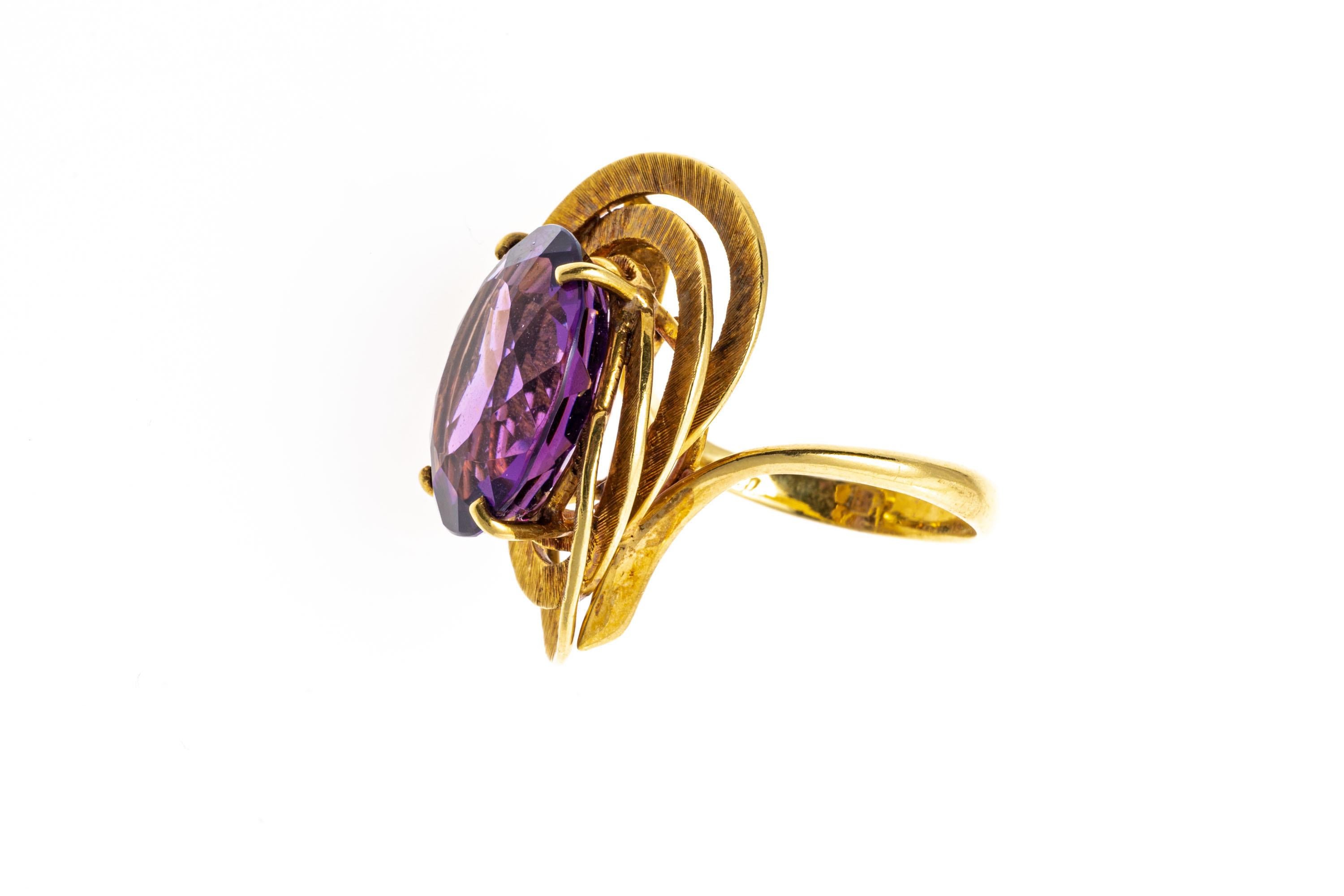 18k yellow gold ring. This eye-catching vintage ring has an oval faceted, medium to dark purple color amethyst, approximately 7.60 CTS and prong set into a bypass style shank, and decorated with a triple frame of flat, tooled wide rings.
Marks: