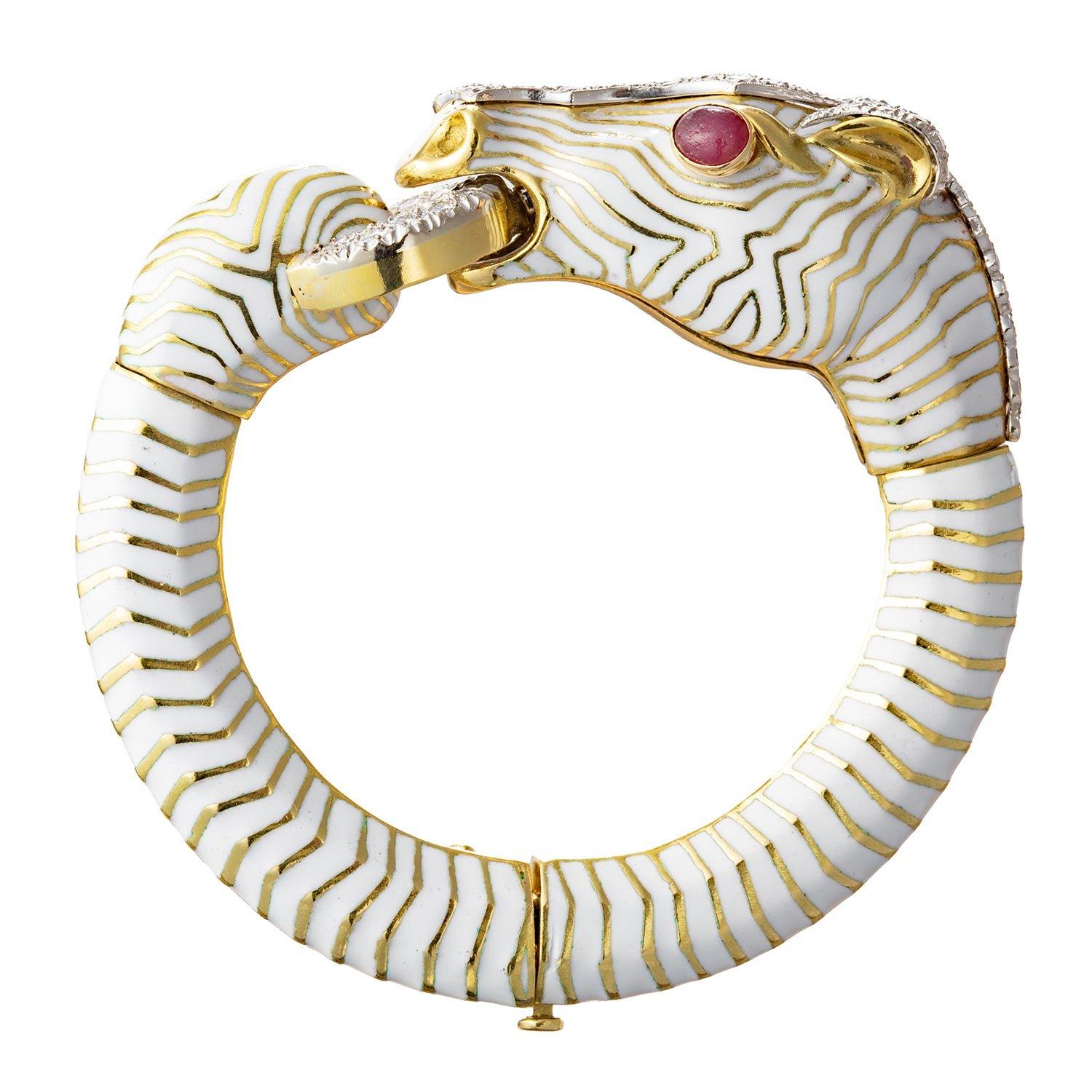 Bracciale bangle a forma di cavallo stilizzato, con smalto bianco a righe impreziosito da diamanti rotondi incastonati a pavé alla sommità della testa, della criniera e del morso, oltre a occhi ovali cabochon di rubino. Realizzato a mano in oro