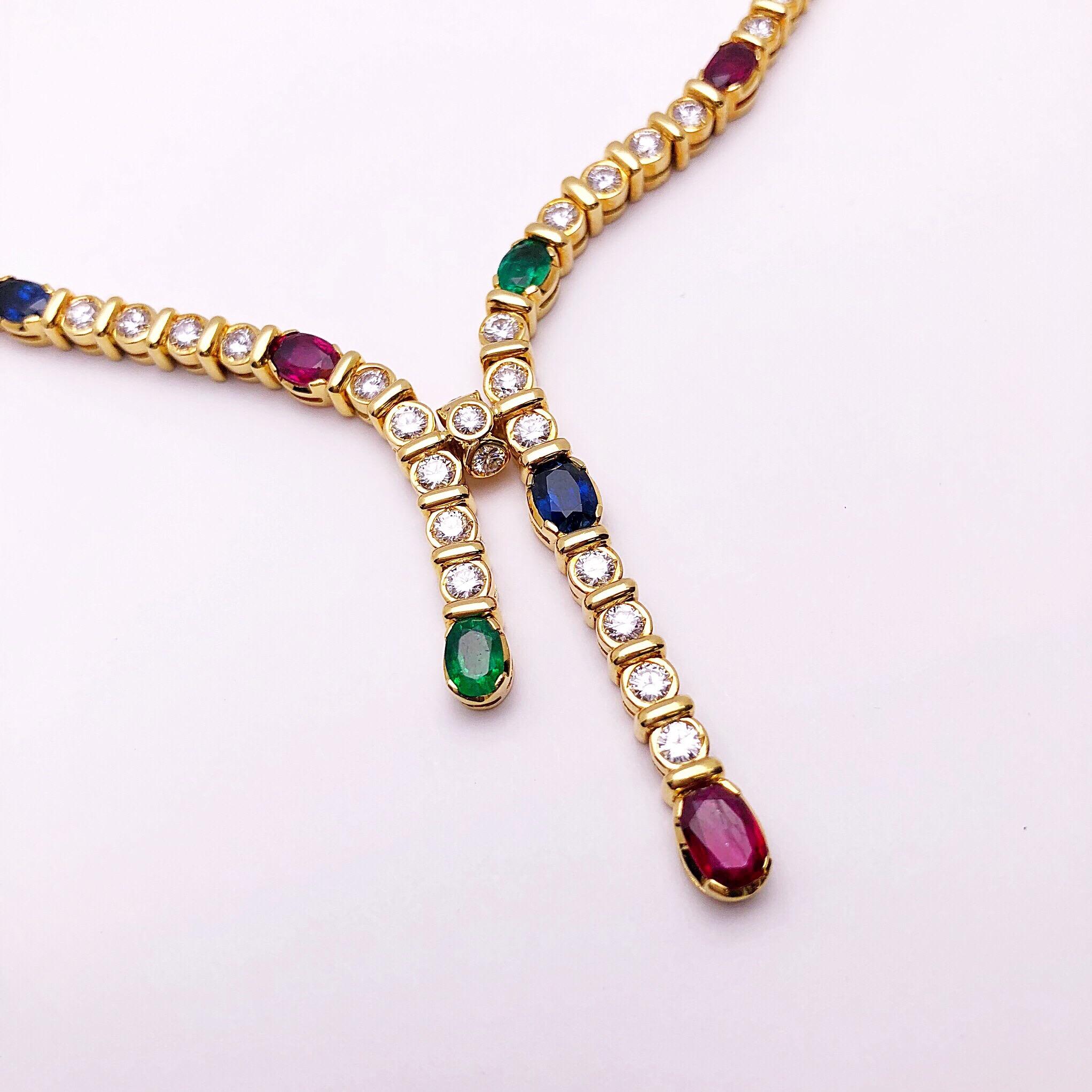 Round white brilliant diamonds alternating with oval rubies, emeralds and sapphires makeup the composition of this beautiful necklace. 
The 18 karat yellow gold necklace is bezel set, along with a lariat style, allowing the diamonds and gem stones