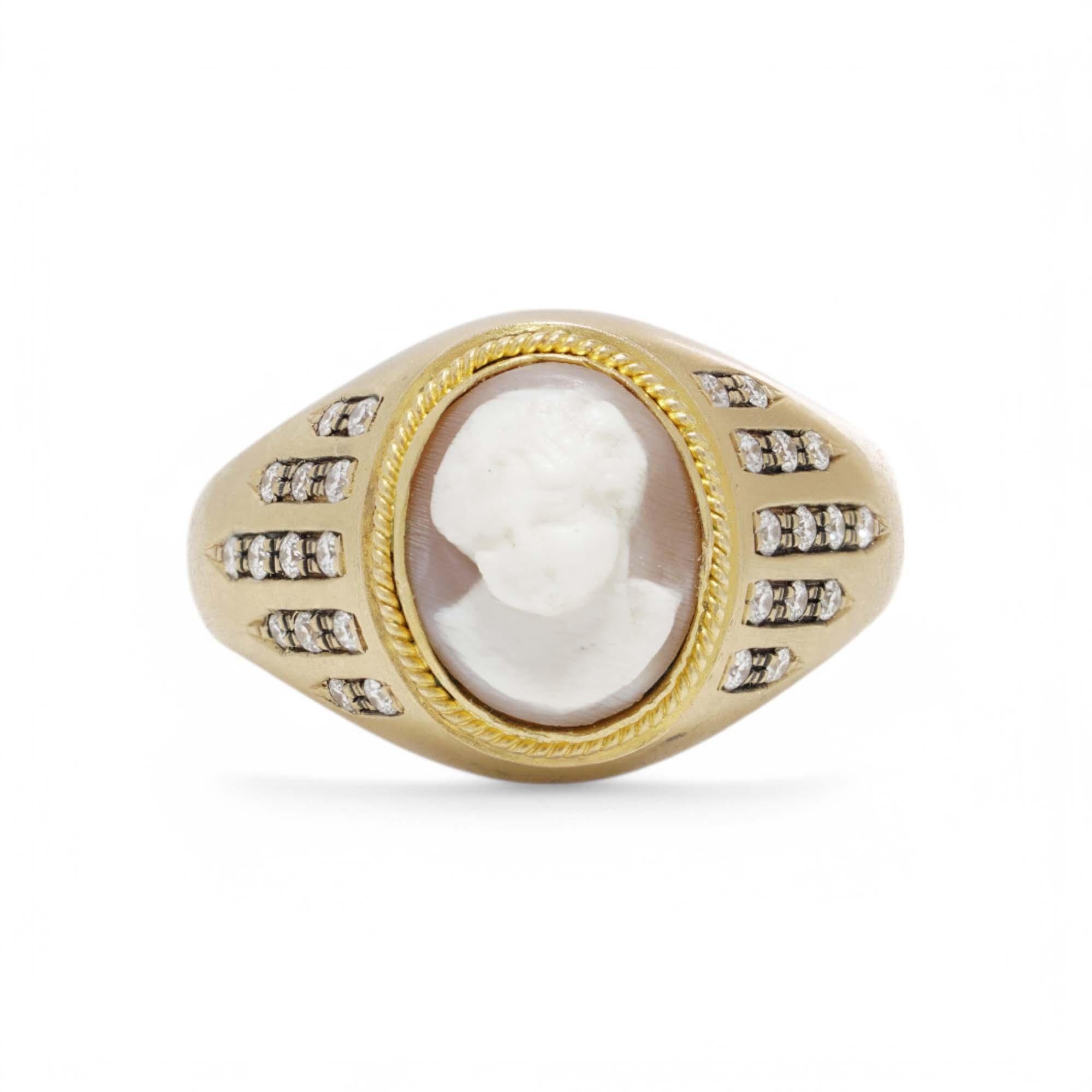 A finely crafted 18kt yellow gold ring featuring an intricately carved white cameo depicting a classical profile. The cameo is framed with a delicate gold beaded border, enhancing its refined elegance. The shoulders of the ring are adorned with