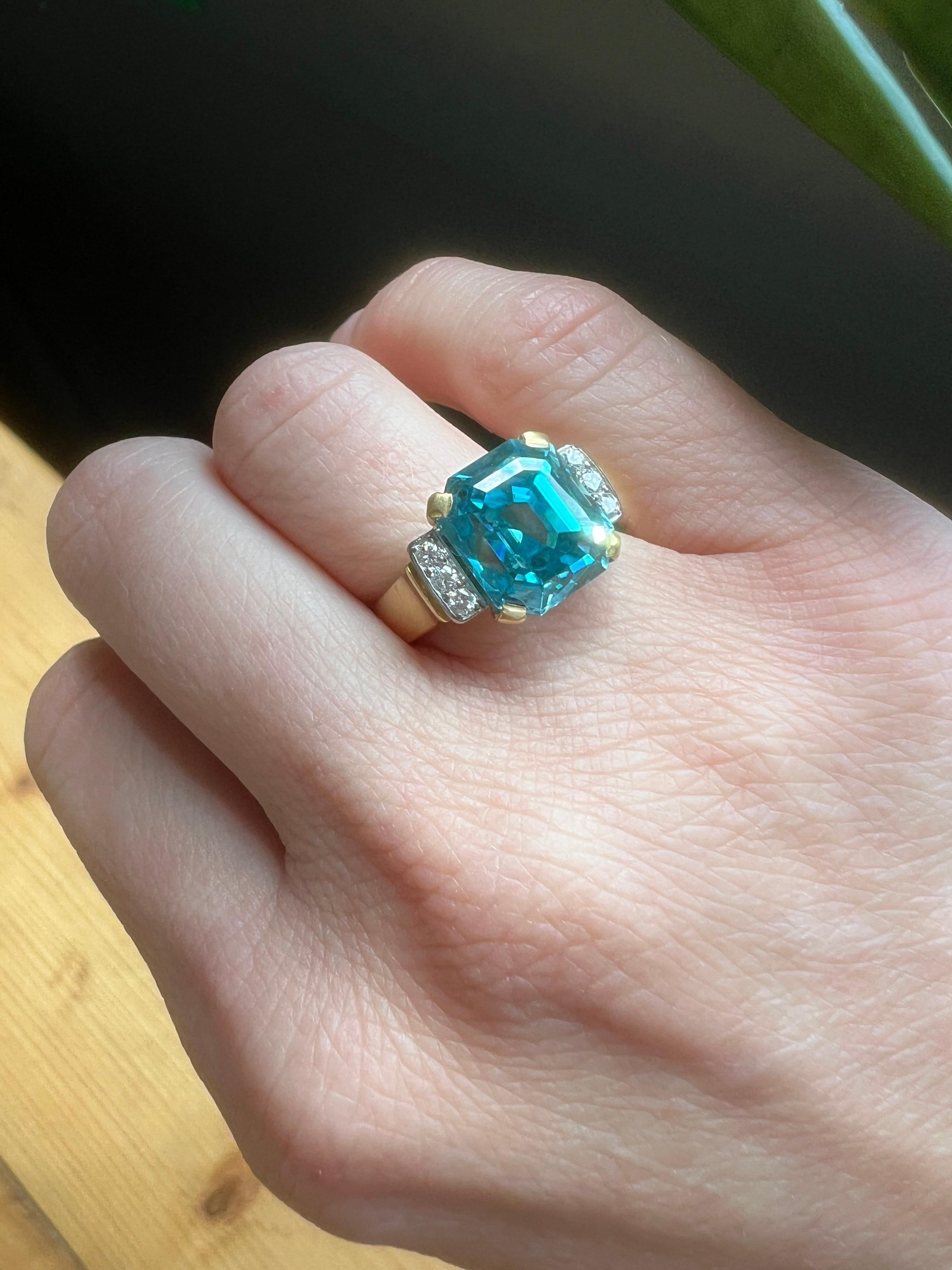18kt Gold Blue Zircon Ring with Diamond Accents by Adamek
Circa 1990's

Weight: 7.51 grams
Dimensions: 27 x 20 x 12 mm
Finger Size: UK N (US 6 3/4, EU 54)

Gemstones:

Center Stone: Approx. 4.8 ct natural blue zircon, radiant cut

Diamond Accents: