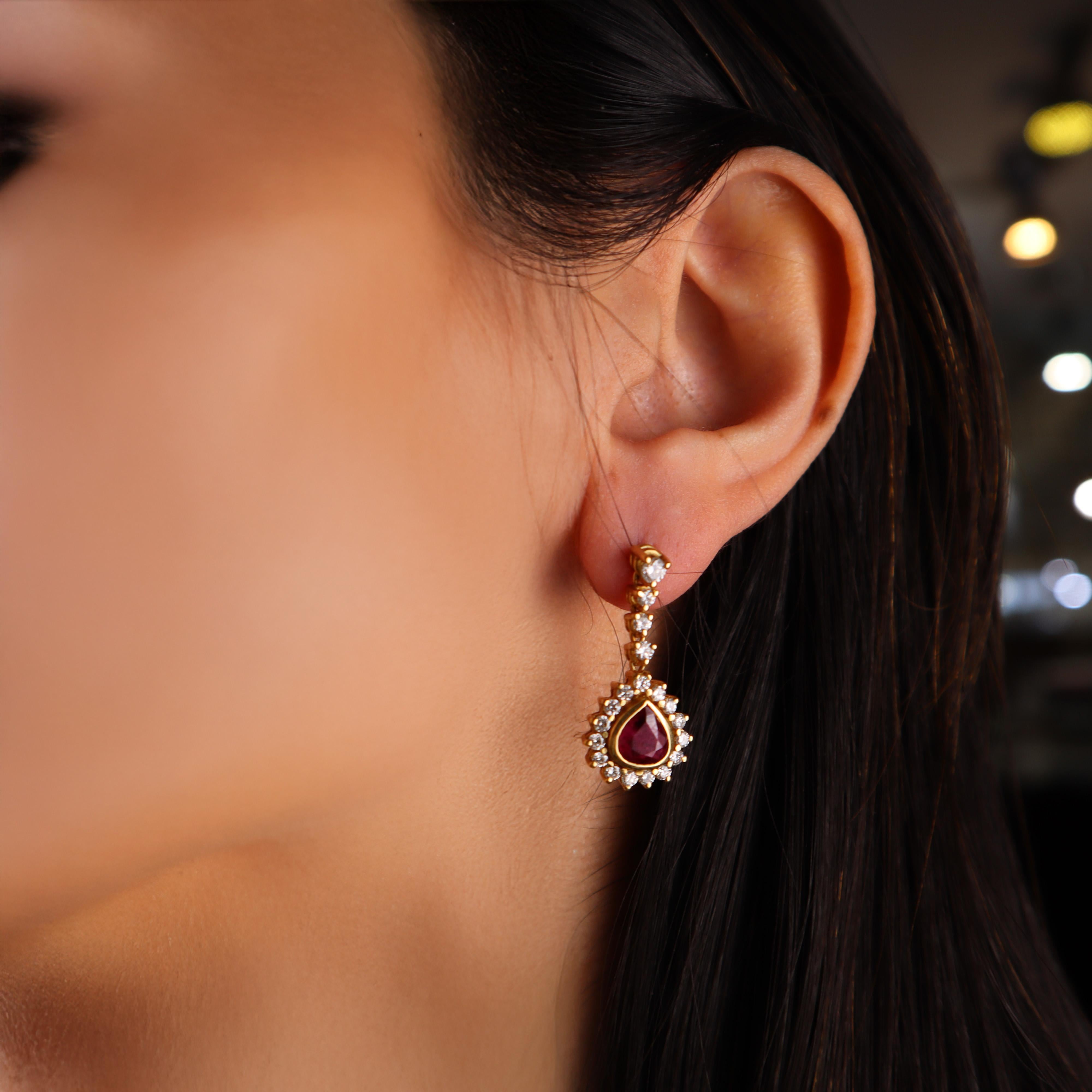 This exquisite pair of drop earrings is crafted in 18kt yellow gold, featuring a stunning combination of precious gemstones. The centerpiece of each earring is a gem-quality, pear-shaped ruby, weighing a total of approximately 4.00 carats. These