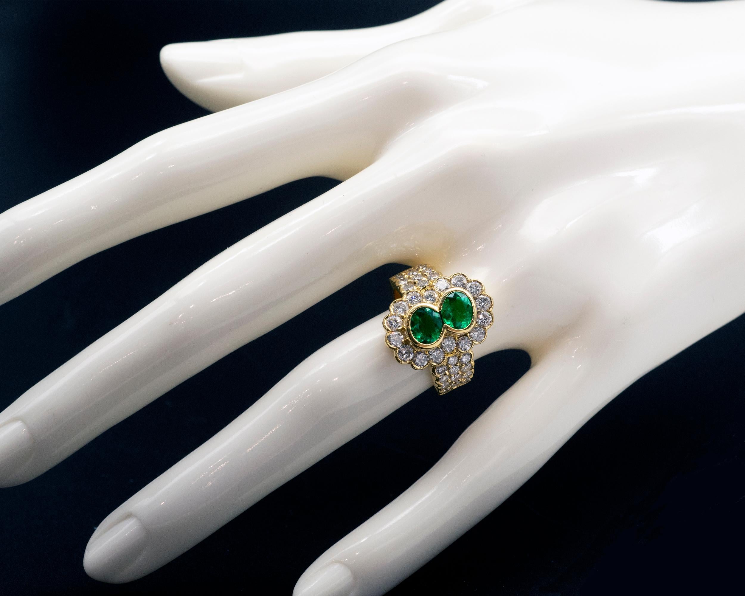 It is an opulent emerald ring showcasing two vibrant green oval emeralds. It is a one-of-a-kind halo ring with round brilliant cut diamonds skilfully set around the center gemstones as well as on the shaft. The whole ring is handmade in solid 18
