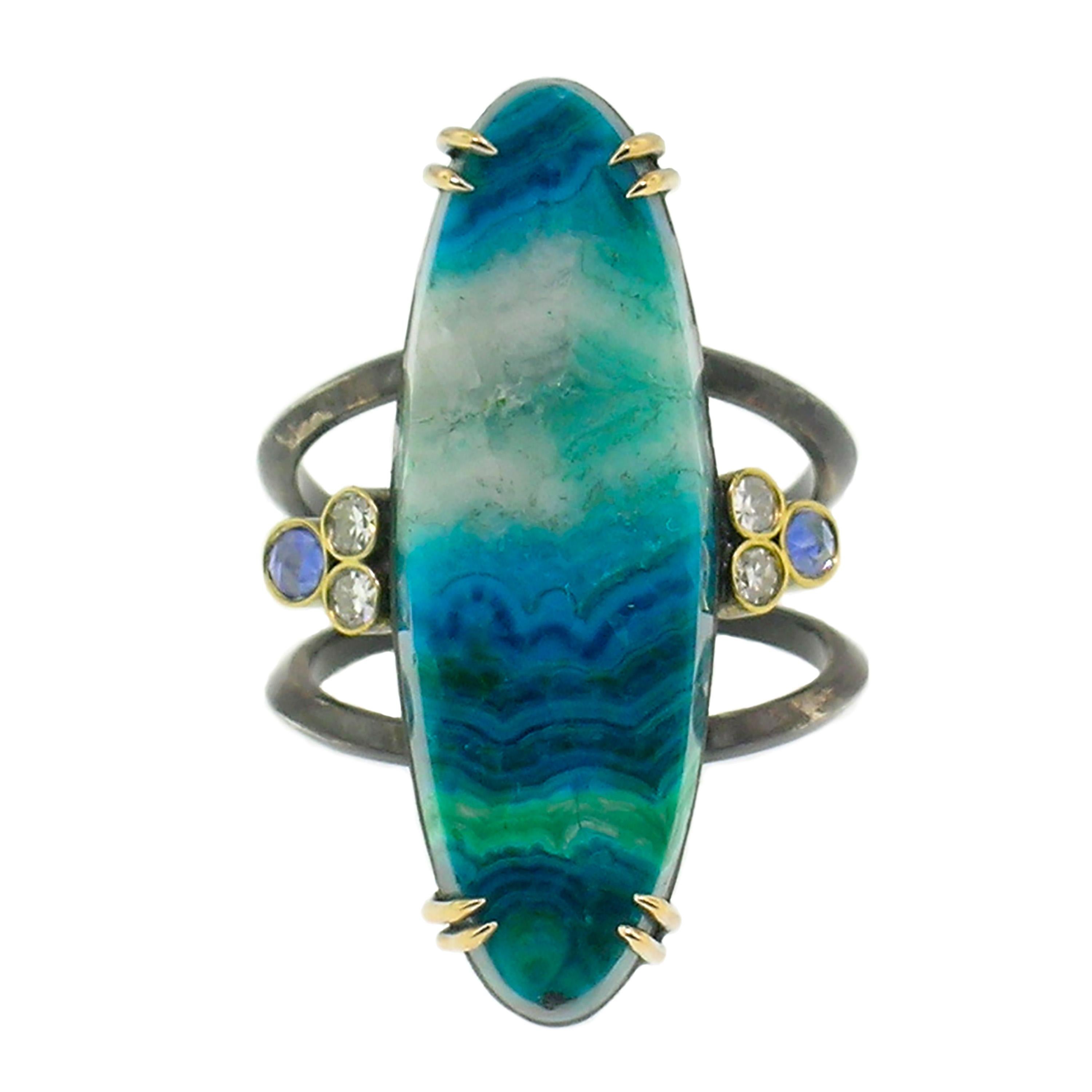 This Shield Ring features a unique specimen of Malachite and Chrysocolla with Quartz from Arizona, chosen for its elegant bands of color and elongated oval shape. The center gemstone is flanked by rose cut blue sapphires and diamonds. 

Shield Rings
