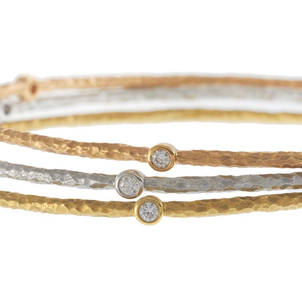 This refined set of three bangles showcases the harmony of 18KT yellow, white, and rose gold, each accented with bezel-set round brilliant diamonds. The hammered finish gives a subtle texture, while the scattered diamonds add a touch of sparkle