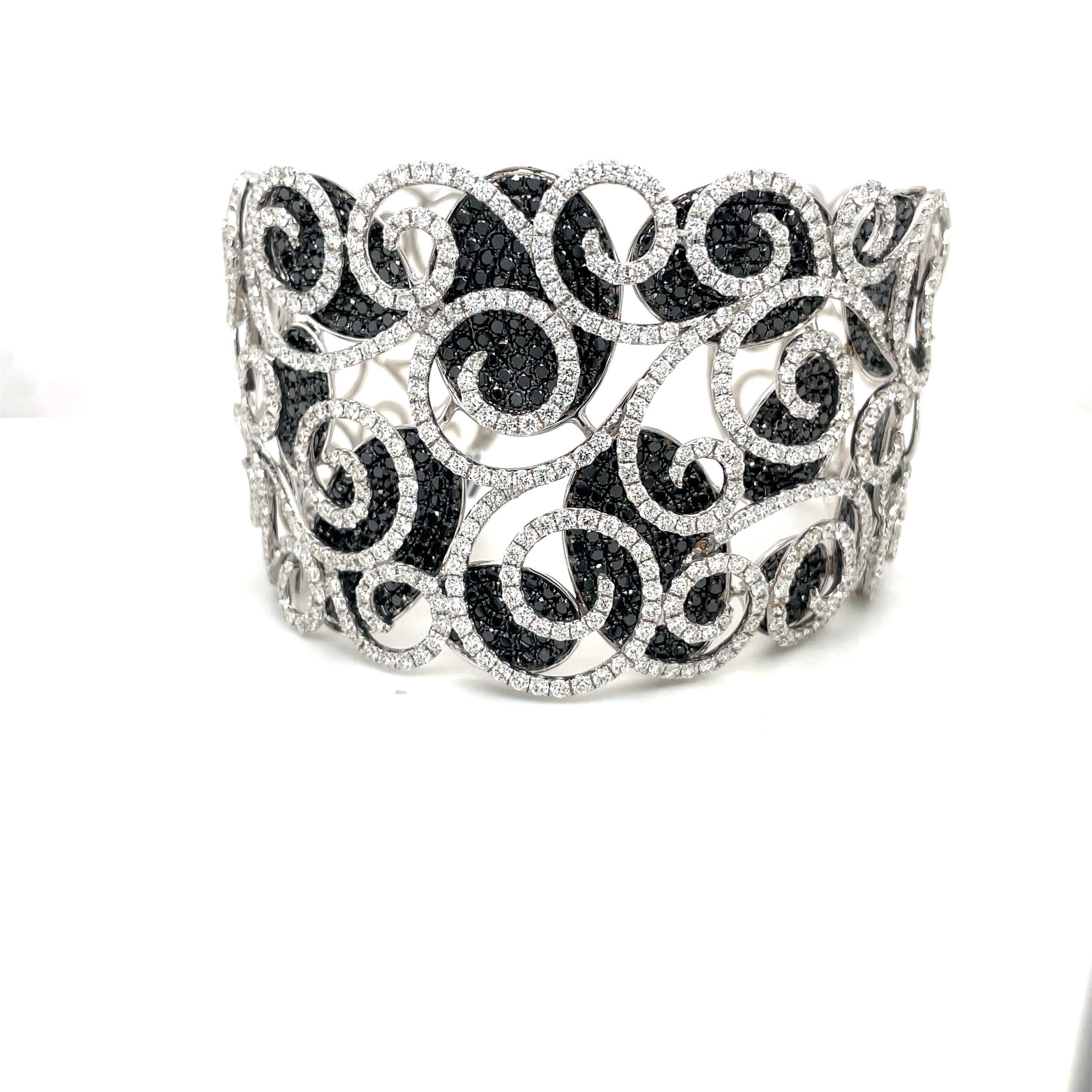 Black and white diamond pavé open-scroll motif cuff bracelet. Set in 18-karat white gold, the white diamonds are set in a scroll pattern which overlay the black diamond ovals. The cuff is 1.75