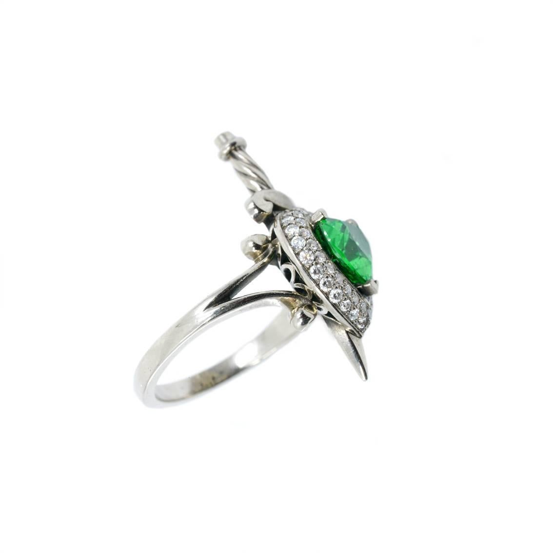 This luxurious Heart and Dagger ring has been handmade from 18kt white gold and features a central, heart cut, Tsavorite garnet, approximately 1.50ct in weight and vivid green in colour. 

A vibrant halo surrounds this astounding stone, made up of