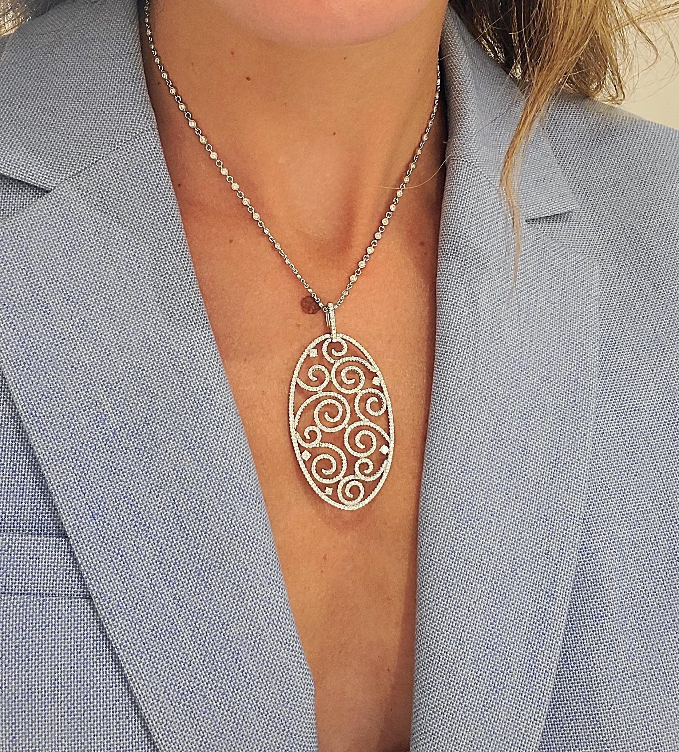 This 18 karat white gold oval  pendant is set entirely with round brilliant Diamonds in a swirly pattern. The pendant hangs from a 16