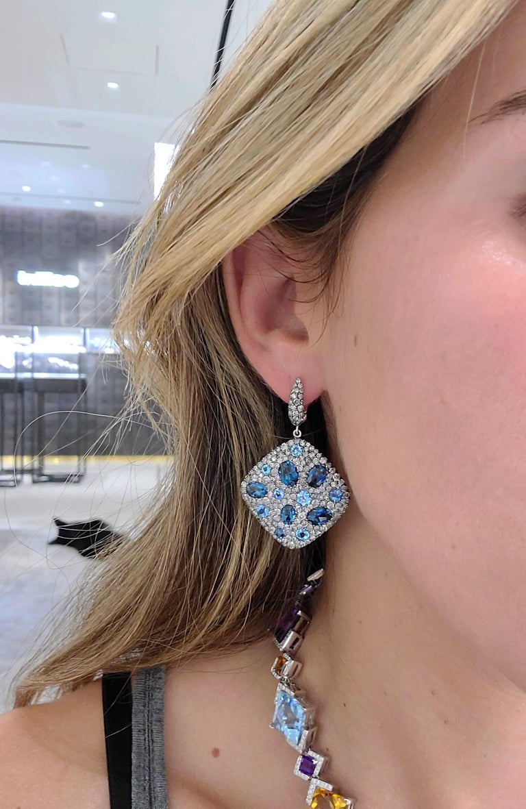 18 karat white gold square cushion shaped hanging earrings. These earrings are pave set with round silver grey diamonds. Oval and round blue topaz stones are set within the diamonds for a beautiful contrast. The earrings measures 1.25