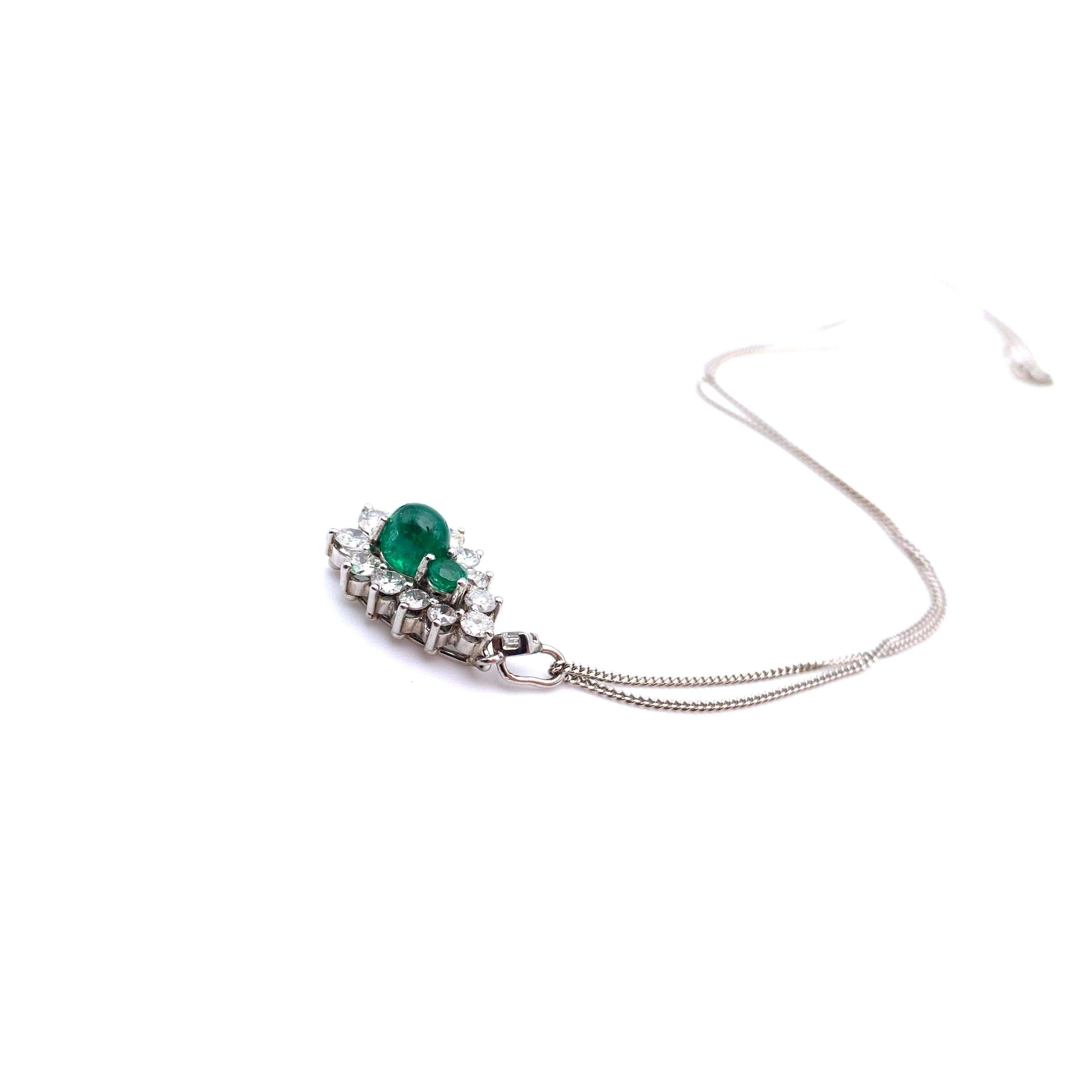 This necklace is part of our estate collection. It is a classic halo design set in 18-karat white gold. The center stones are two emeralds- the larger stone is cut en cabochon and the smaller is faceted to present the illusion of a larger, pear-cut