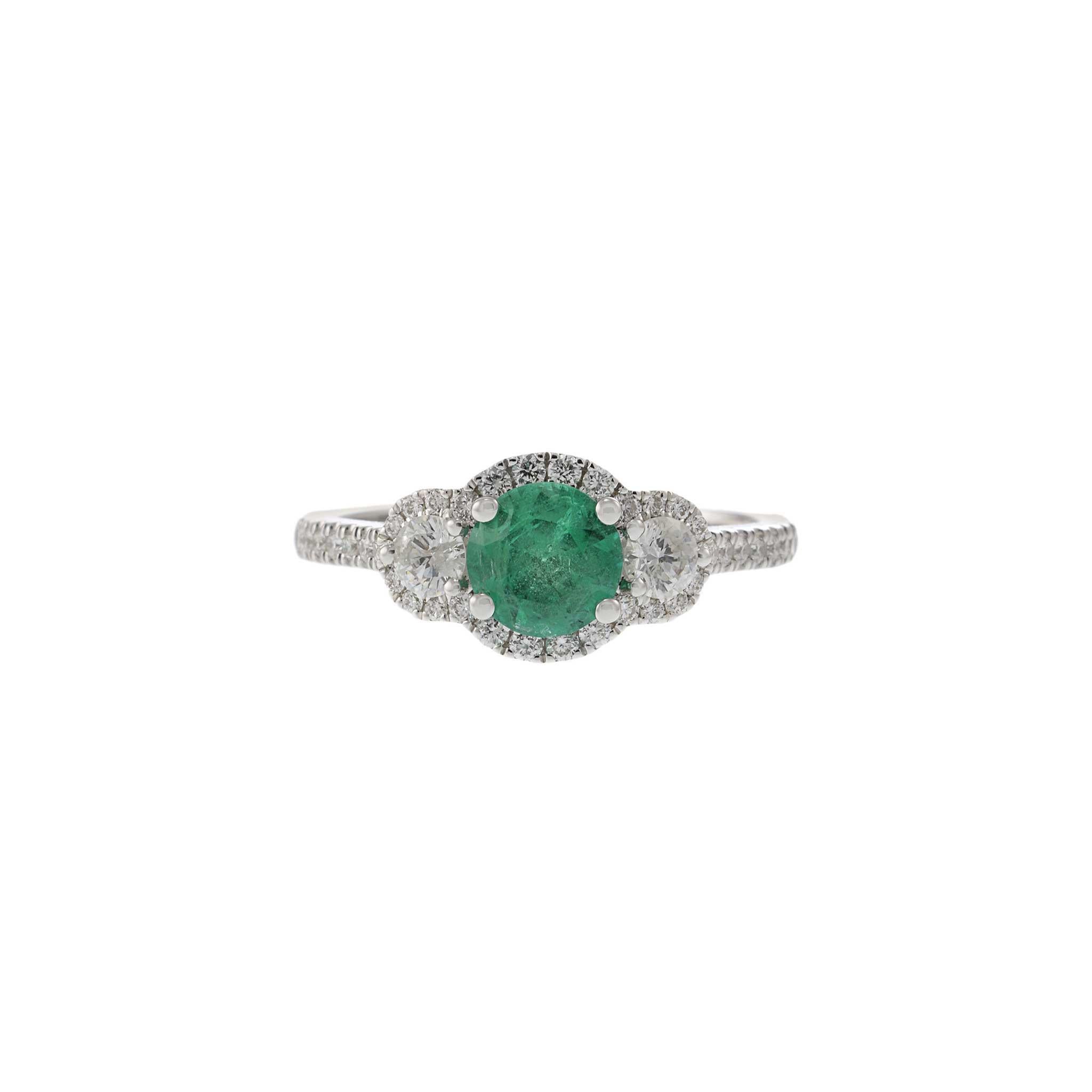 This elegant three stone ring features a 0.69 carat round cut emerald, beautifully set in 18KT white gold. The emerald is flanked by two round cut diamonds, with additional round cut diamonds adorning the band, totaling 0.55 carats with G-VS