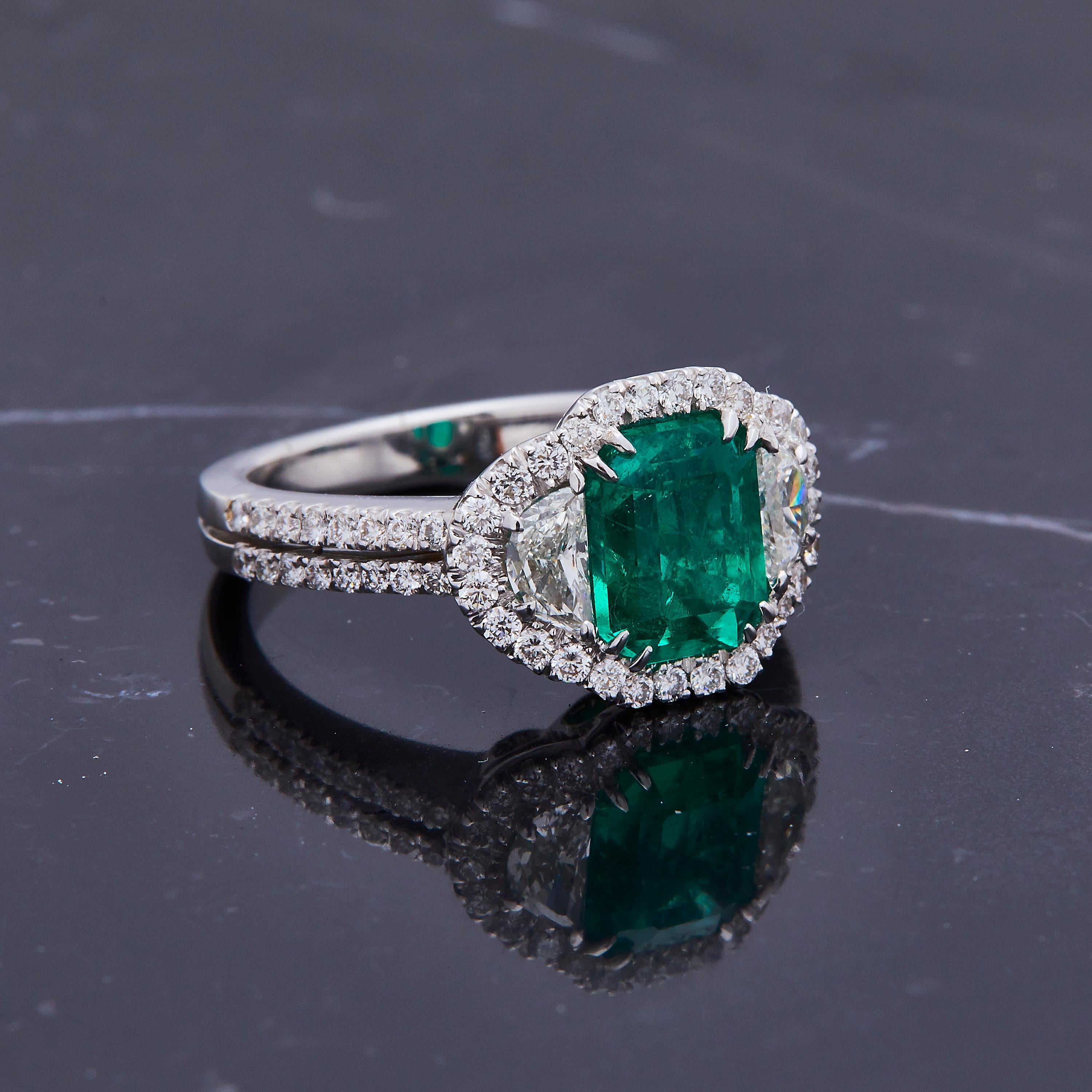 This modern classic ring features a 2.31ct lustrous high quality emerald. The center stone is flanked by gorgeous half moon diamonds on each side with a halo bordering around the edges and diamonds running down the double band. Its so timeless it