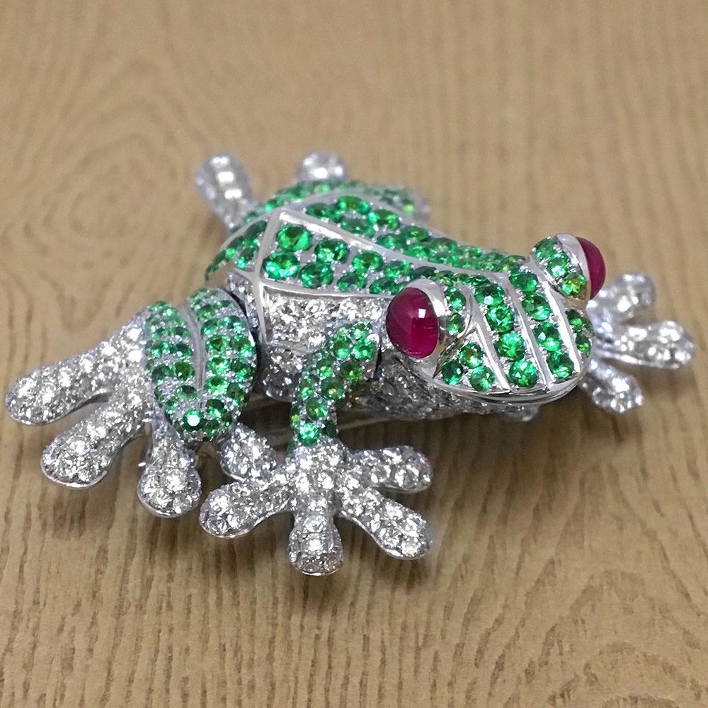 This adorable 18 karat white gold frog brooch is set with 1.70 carats of round Brilliant Tsavorites. His feet are set with round Brilliant Diamonds. Two Ruby Cabochons are set for the eyes. The frog measures 1