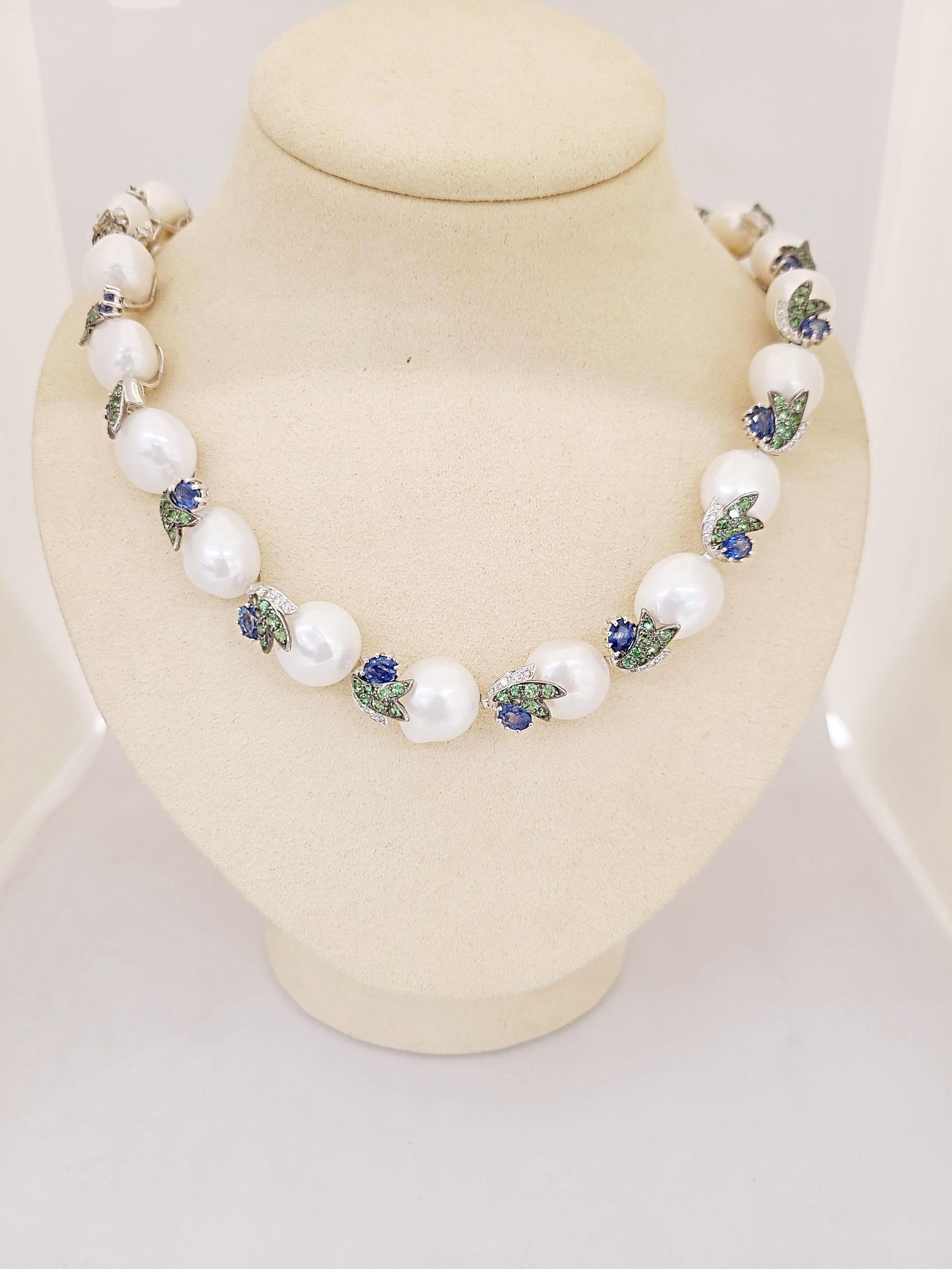 This beautiful 18 karat white gold collar necklace is designed with 22 semi Baroque Pearls , approximately 12mm. each. The pearls are connected by 18 kt white gold leaf sections with Diamonds and Tsavorites and a round Blue Sapphire. The total
