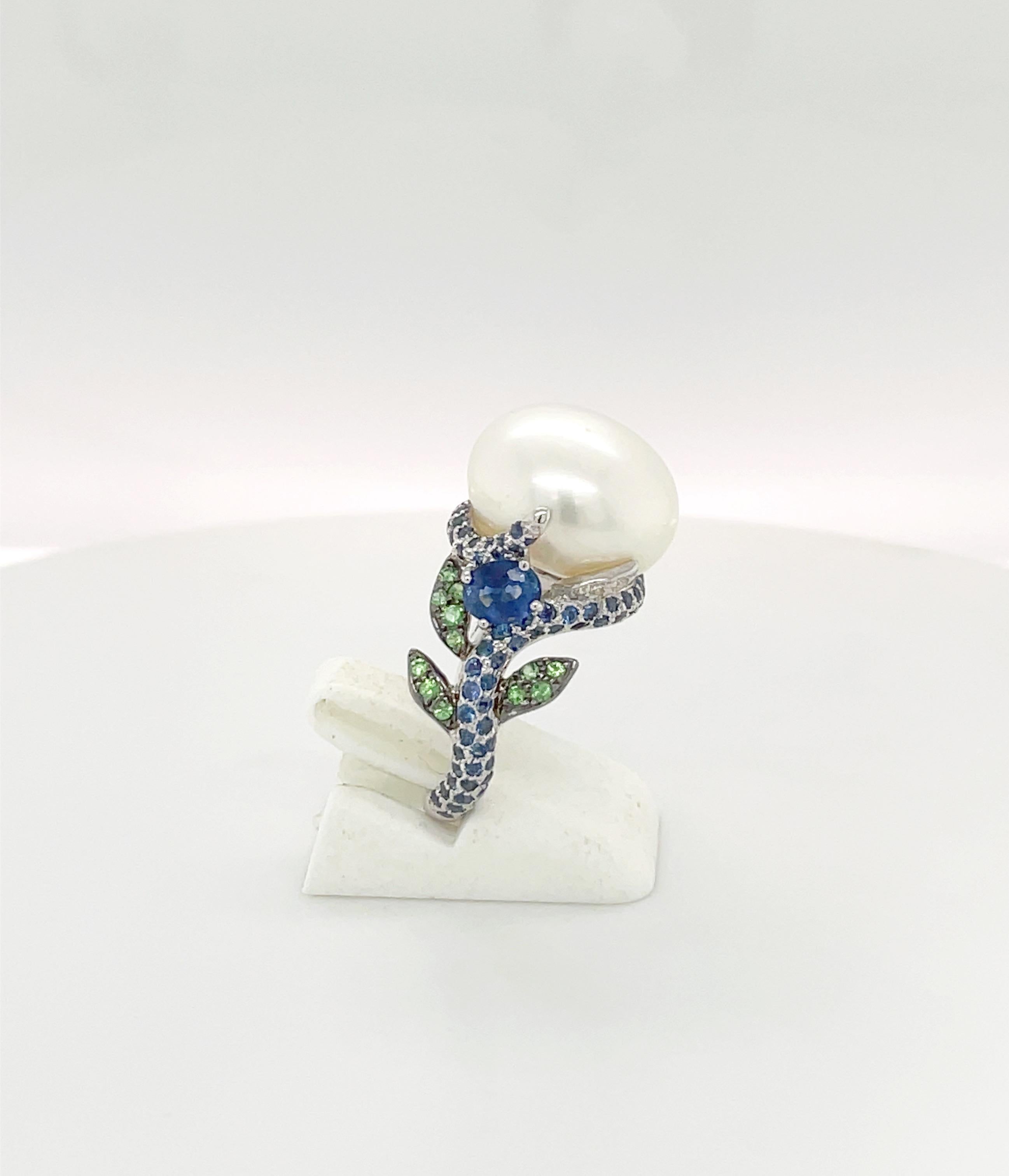 A lovely designed ring centering a 14.5 x 10.5 mm pearl. The 18 karat white gold setting is set with round blue sapphires all along the shank. Green tsavorites and diamonds are set as leaves along with a larger blue sapphire on either side.
Blue