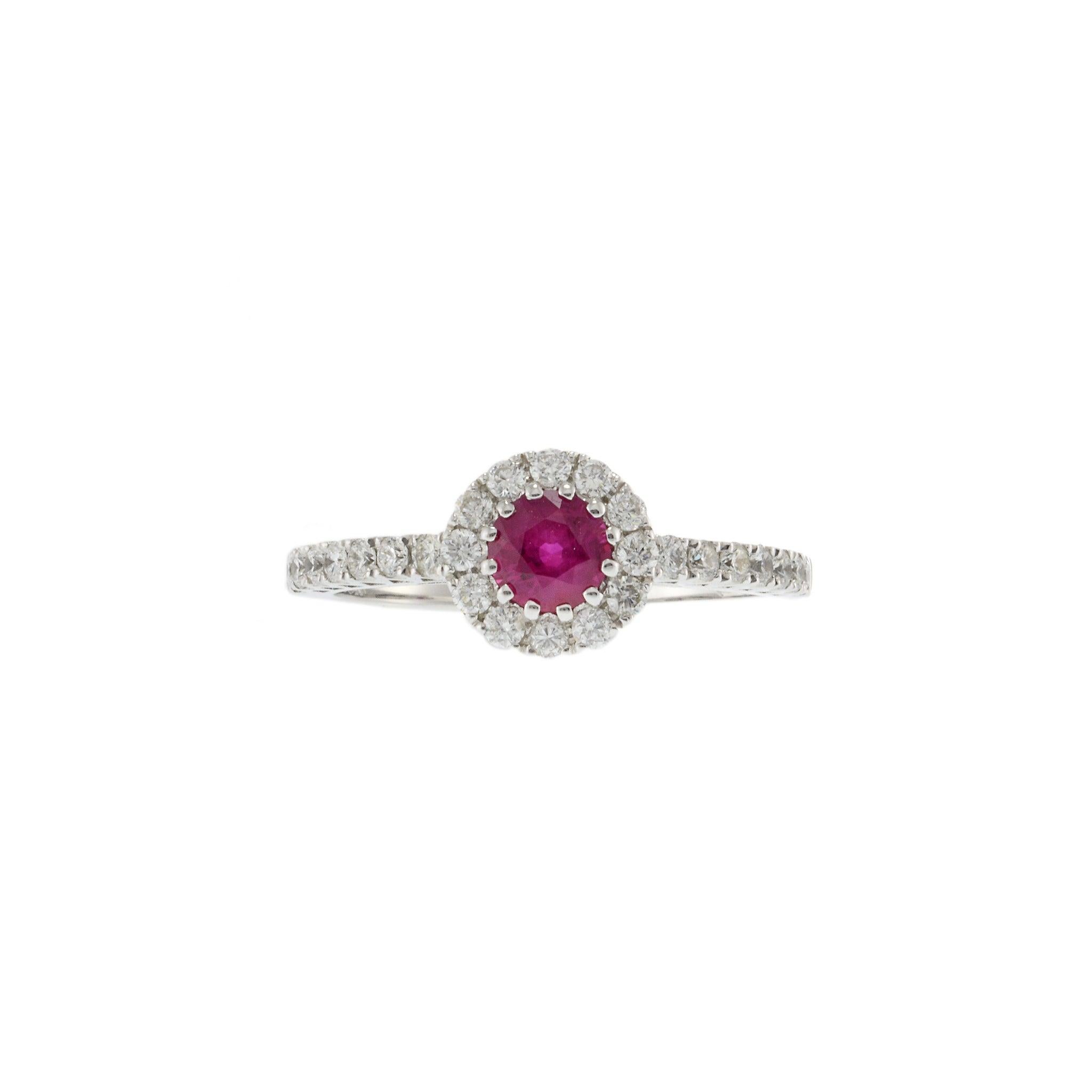 18KT White Gold Ruby Halo Diamond Ring. This elegant ring features a 0.68 carat round brilliant cut ruby, surrounded by 0.48 carats total weight of G-VS round brilliant cut diamonds. Crafted from 18KT white gold and weighing 3.4 grams, this piece