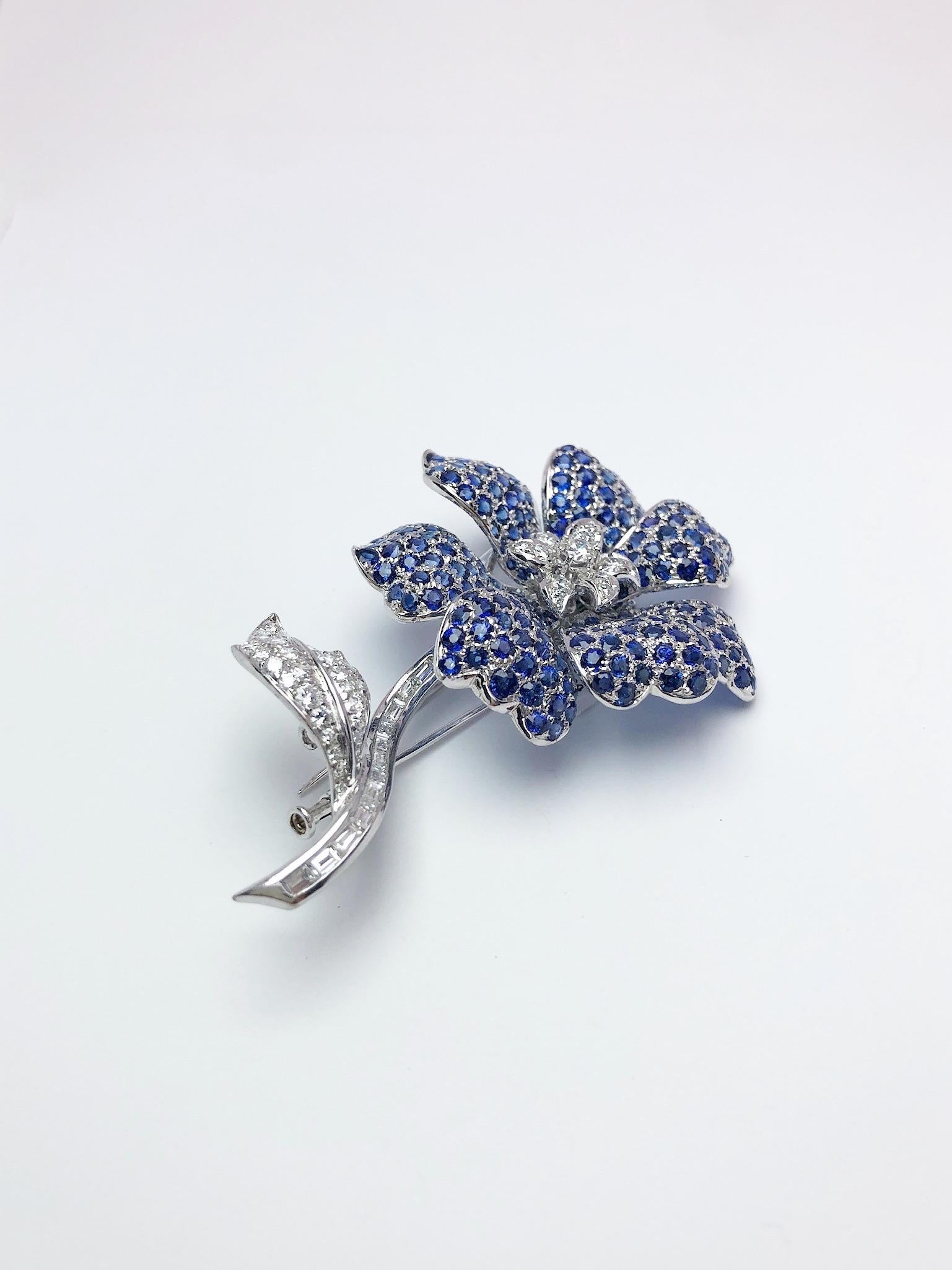 Cellini Jewelers Magnificent 18 karat white gold brooch .The flower is designed with seven petals that are set with round blue sapphires. The center area and the leaves are of round brilliant diamonds, the stem is set with baguette diamonds. The