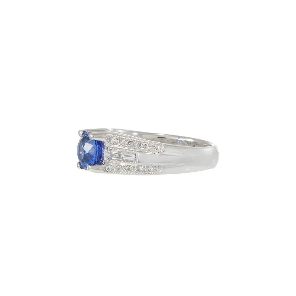 Incastonato in oro bianco lucido 18KT, questo squisito anello mette in mostra un vibrante zaffiro blu a taglio rotondo da 1.67CT come pezzo centrale. A incorniciare la gemma centrale ci sono file di diamanti tondi taglio brillante e baguette, per un