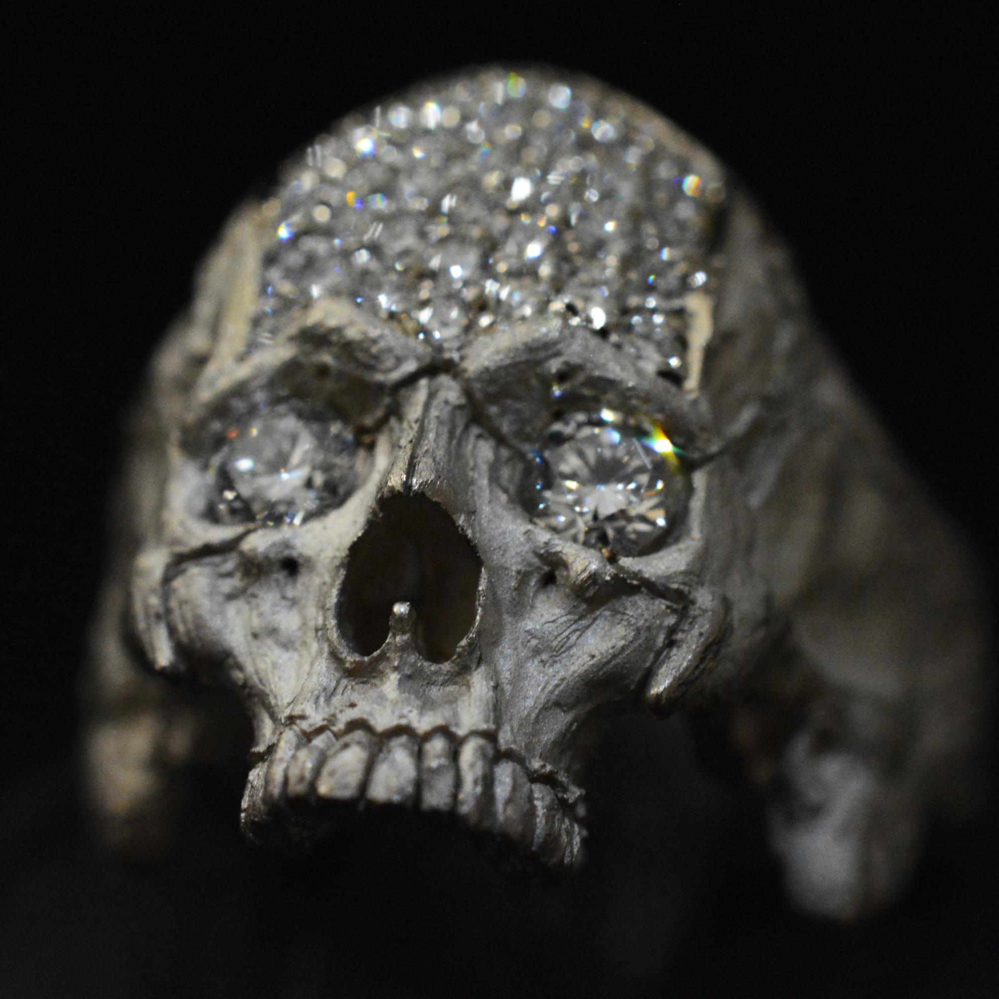 This 18-karat white gold skull ring is a masterpiece of artistry and meaning, blending the raw beauty of precious metals with the profound depth of human existence. The skull, rendered with breathtaking intricacy, features VS1 diamonds set into its