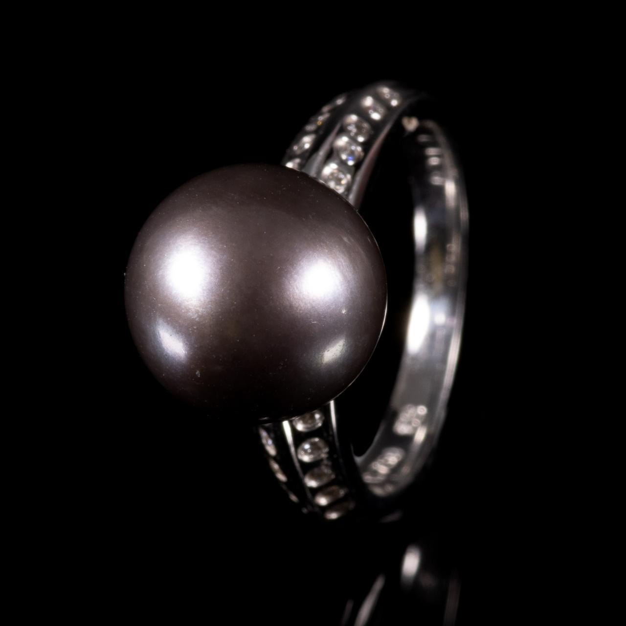 18 Kt. White Gold Tahiti Pearl & Diamond Ring 
Ring set with central black Tahitian pearl, diameter measuring 11mm. 18ct white gold shank set with 20x brilliant-cut diamonds, 0.01ct each, G colour, VS2. 4.56 grams, finger size 15mm.

Good