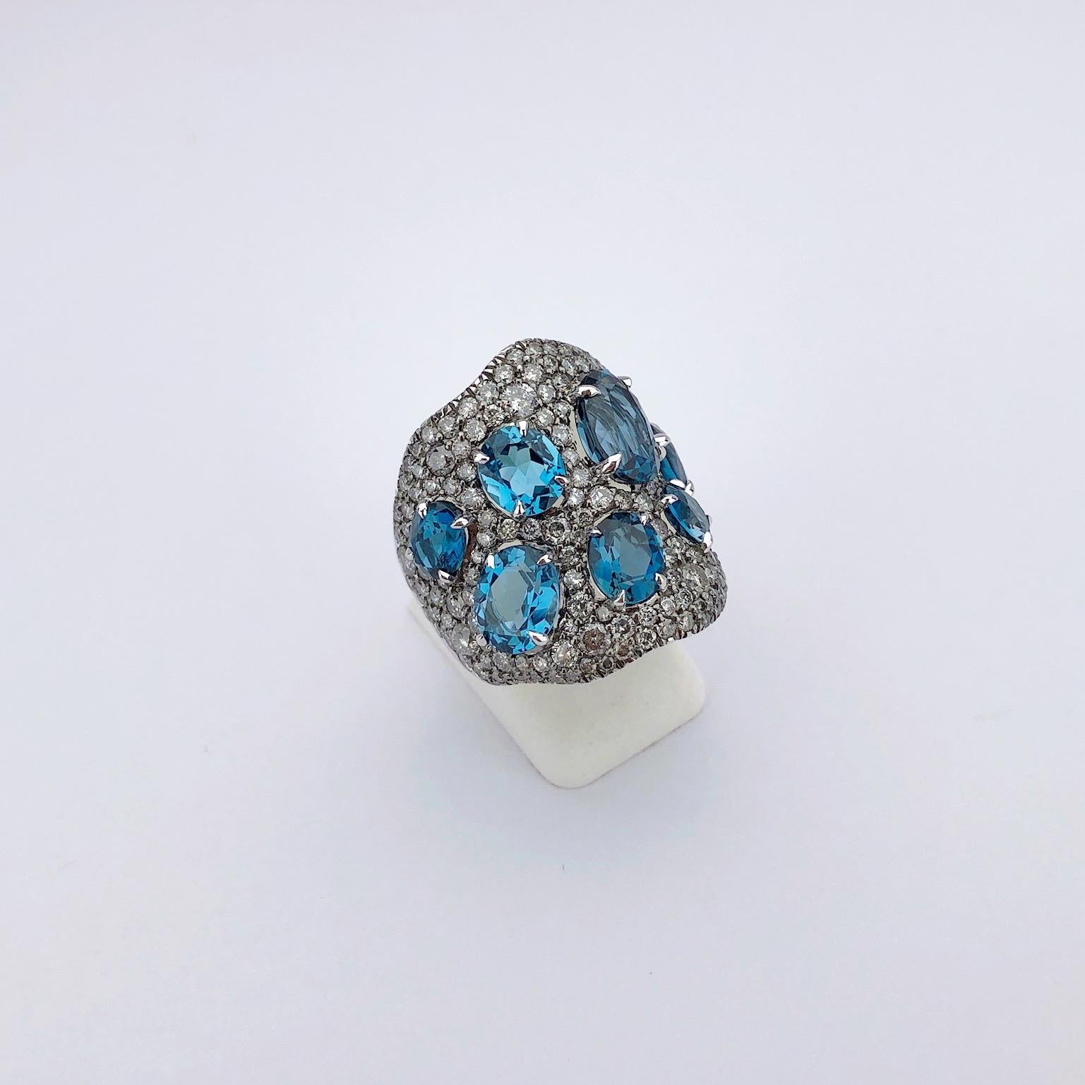 This 18 karat white gold wide wave ring is pave set with silver grey round brilliant diamonds. Oval blue topaz stones are set with the diamonds for a beautiful contrast. The ring measures approximately 1