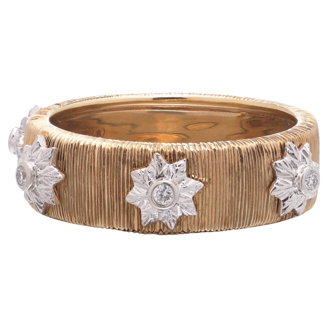 Cette élégante bague en or jaune et blanc 18 carats présente une surface texturée en or jaune rehaussée de quatre sertissages en or blanc en forme d'étoile. Chacune est sertie d'un diamant rond de taille brillant, ce qui ajoute de l'éclat et du