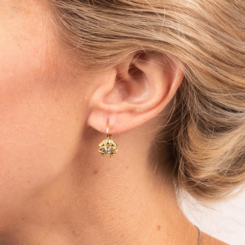 These unique earrings feature two round brilliant cut diamonds in a bezel setting set in 18kt yellow gold with an total carat weight of .09. They have a level back closure and are approximately 1/2