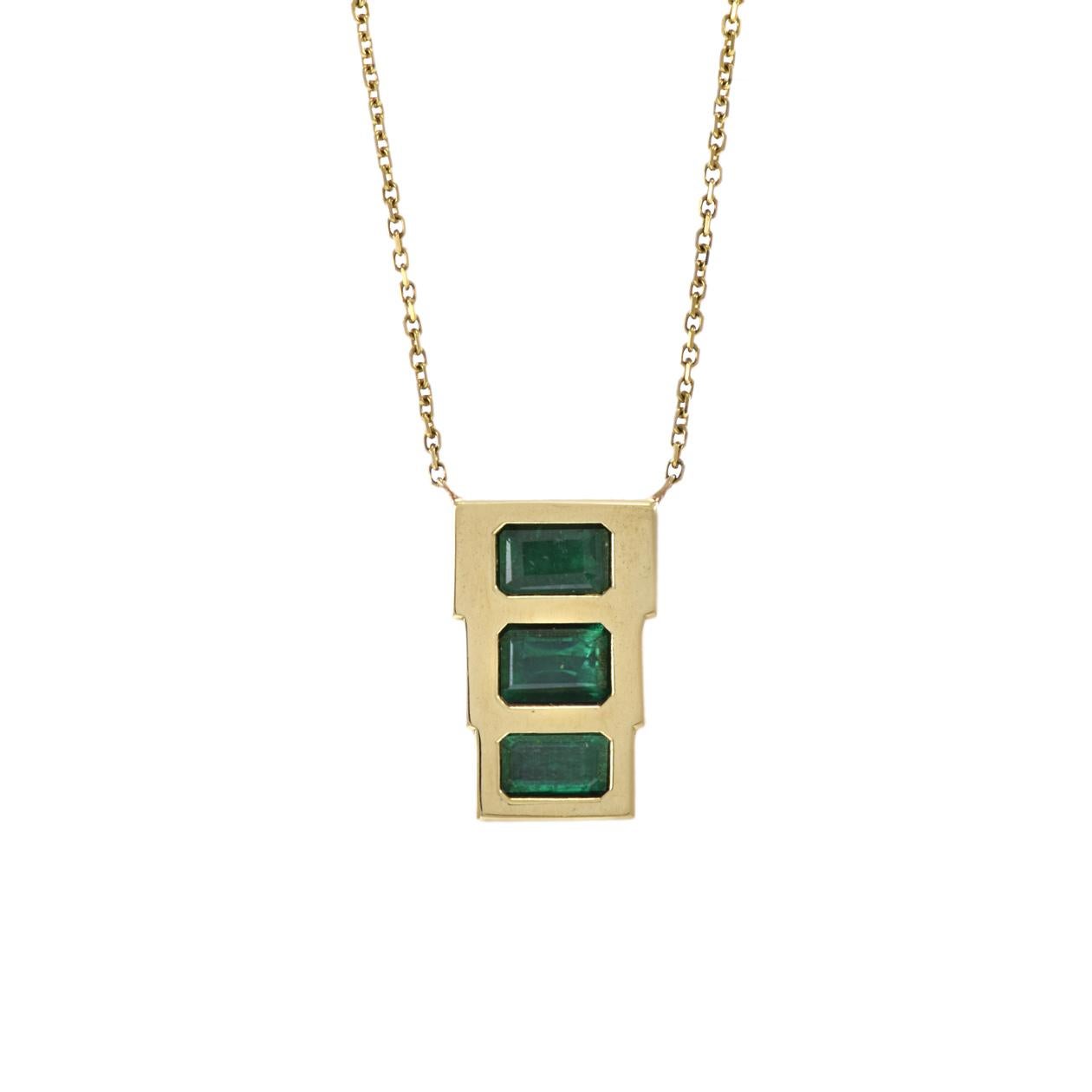 This 18KT yellow gold necklace features three bezel-set rectangular-cut emeralds with a total weight of 1.50 carats. The emeralds are set in a triple arrangement, creating a unique and stylish accessory that adds a touch of vibrant green color and