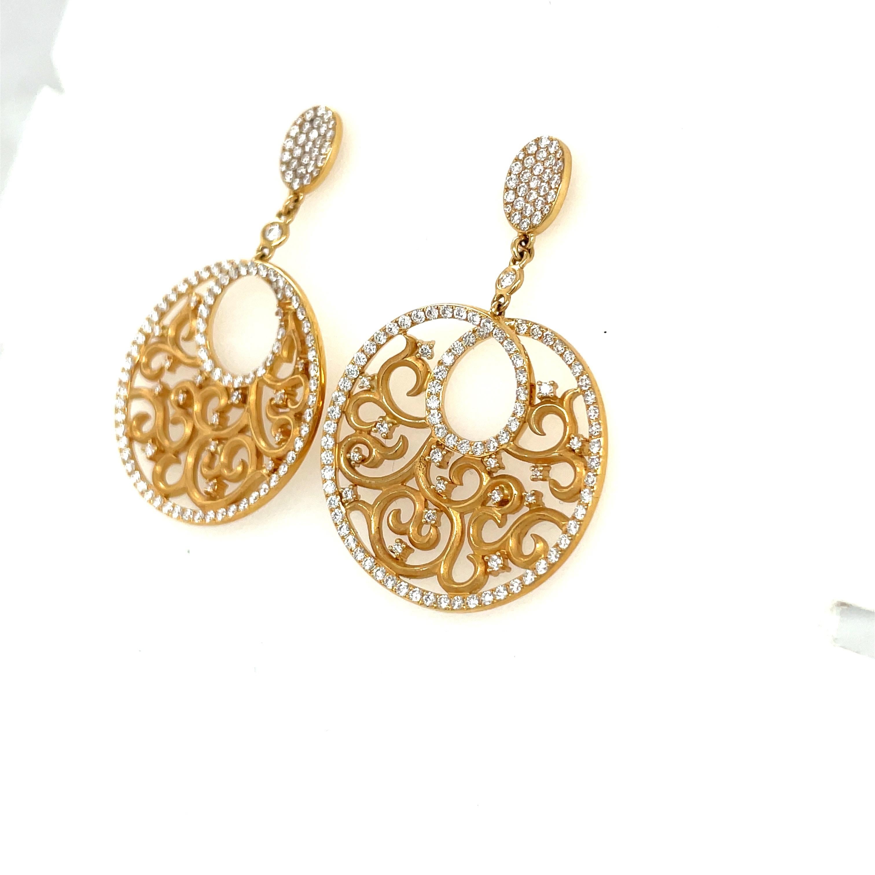 Lovely 18 karat yellow gold hanging earrings. These earrings are designed with a hanging open circle disc which has been cutout and accented with diamonds. The discs are outlined in diamonds hang from a oval pave diamond section. The earrings are