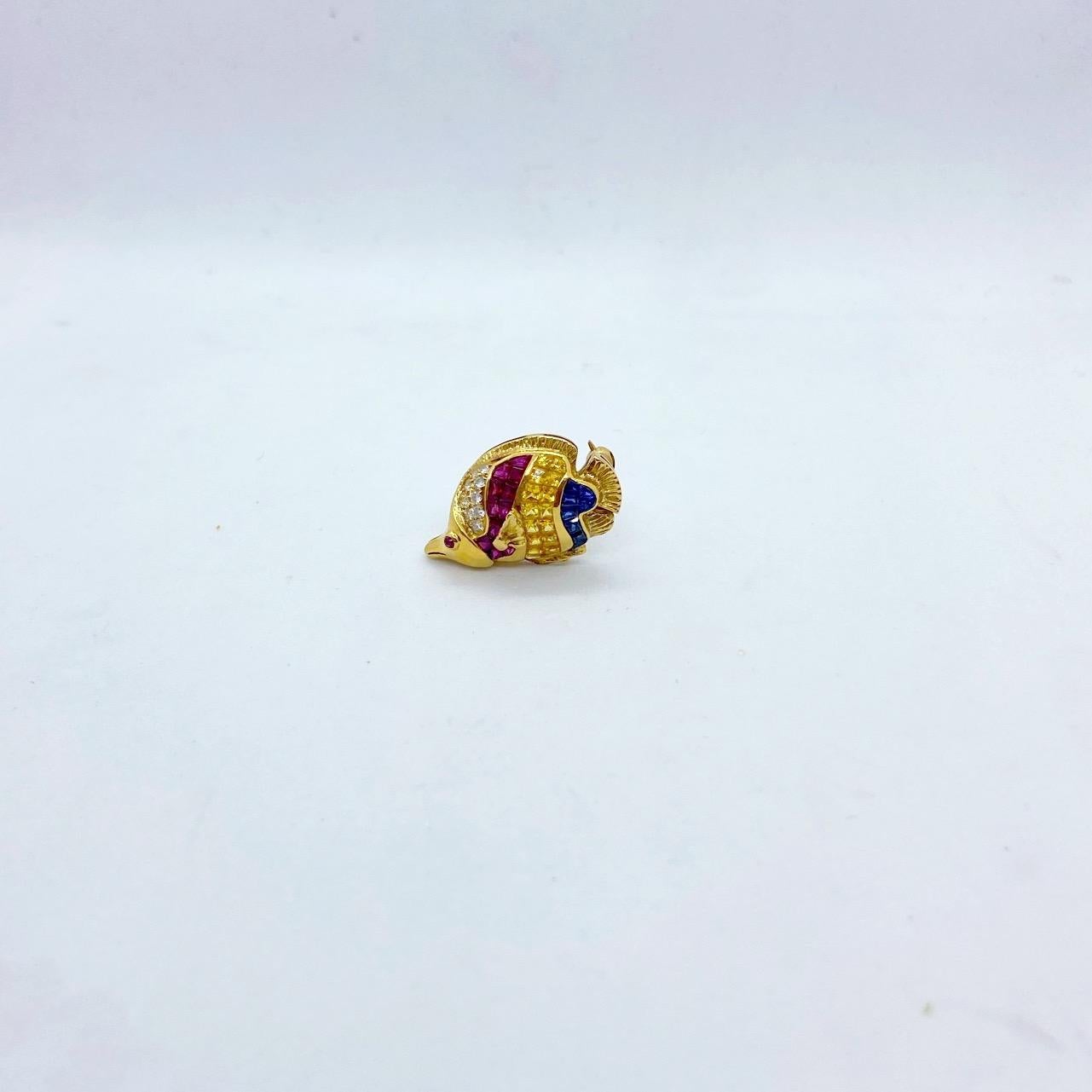 A beautiful interpretation of an angelfish. This 18 karat yellow gold brooch has been invisibly set with square cut rubies,blue and yellow sapphires along with pave set round brilliant diamonds. A cabochon ruby is set for the eye. The fish measures