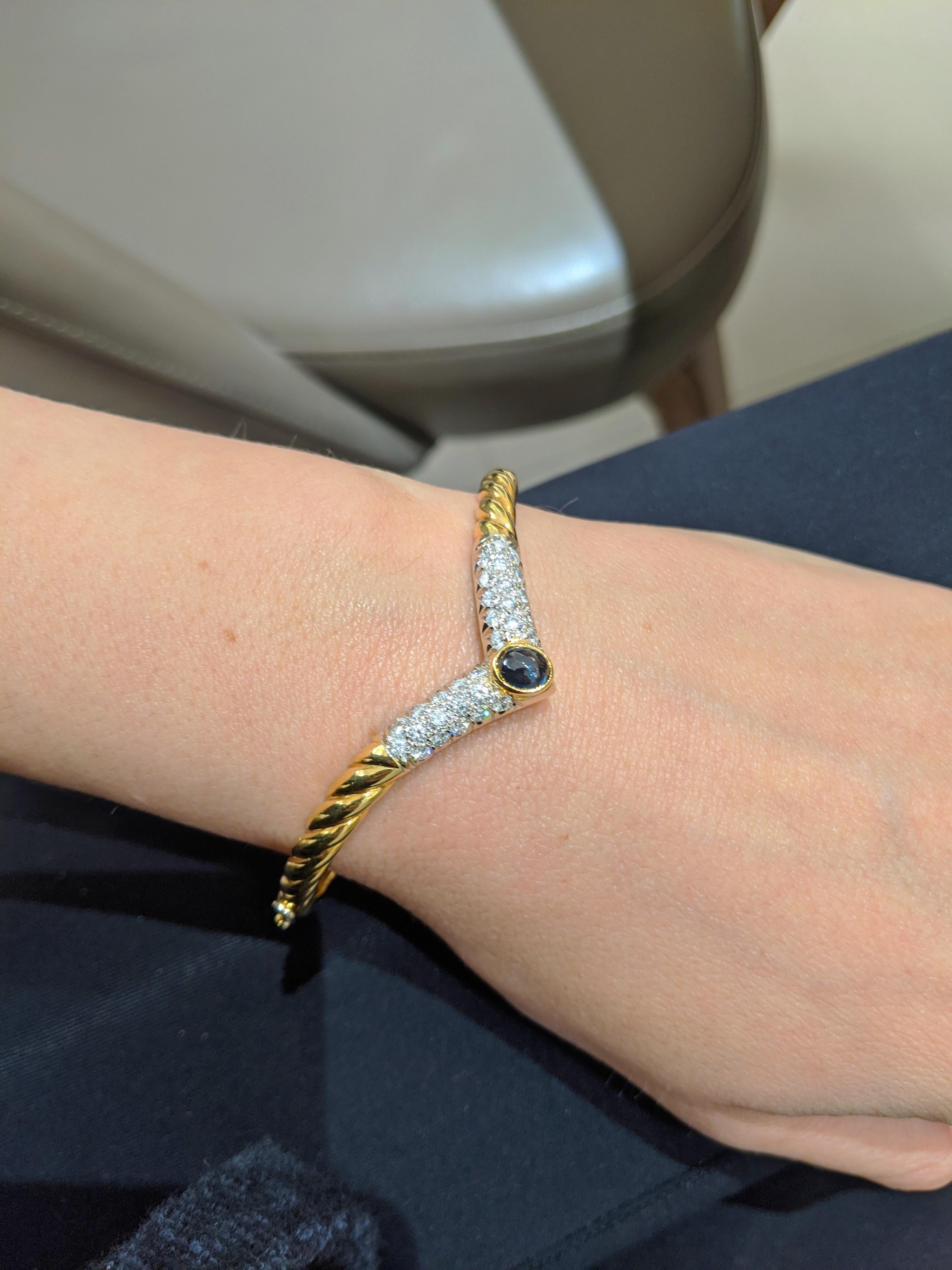 This is a beautiful 18 karat yellow gold bangle bracelet. The Vee shaped bracelet is set with pave diamonds and an oval cabochon blue sapphire. The bracelet measures 2 1/4
