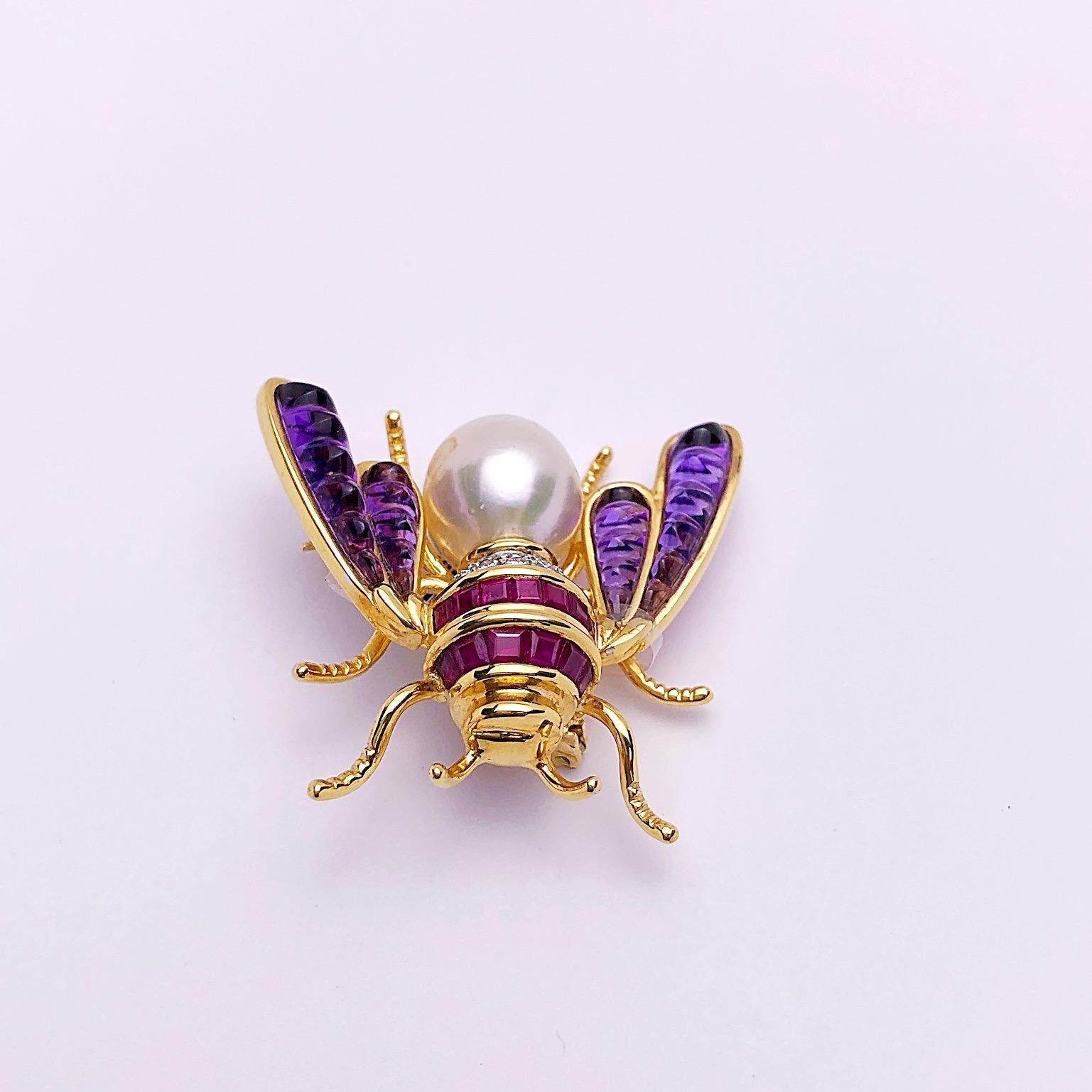 Beautifully detailed 18 karat yellow gold bee brooch. The brooch is intricately set with square cut rubies and round brilliant diamonds. The wings are set with sugarloaf cabochon amethyst and the body is a South Sea pearl.
The brooch measures 1 5/8