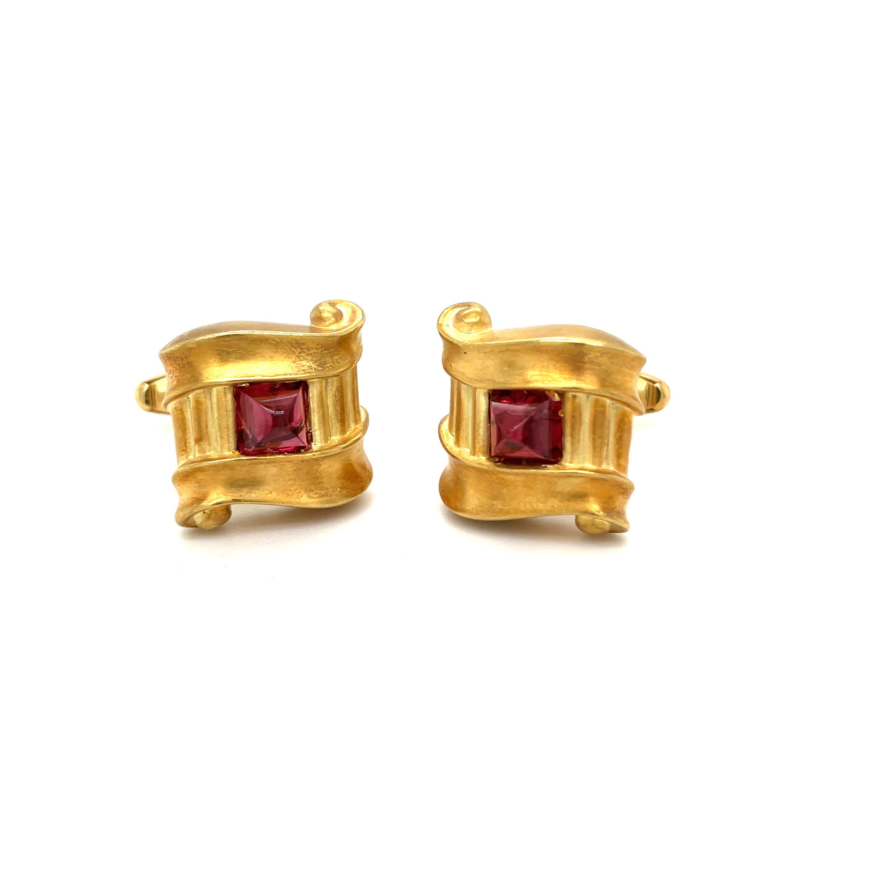 Designed in an 18 karat yellow gold satin finish, these cuff links have rhodolite cabochon centers. The  bar style cuff links measure approximately 3/4