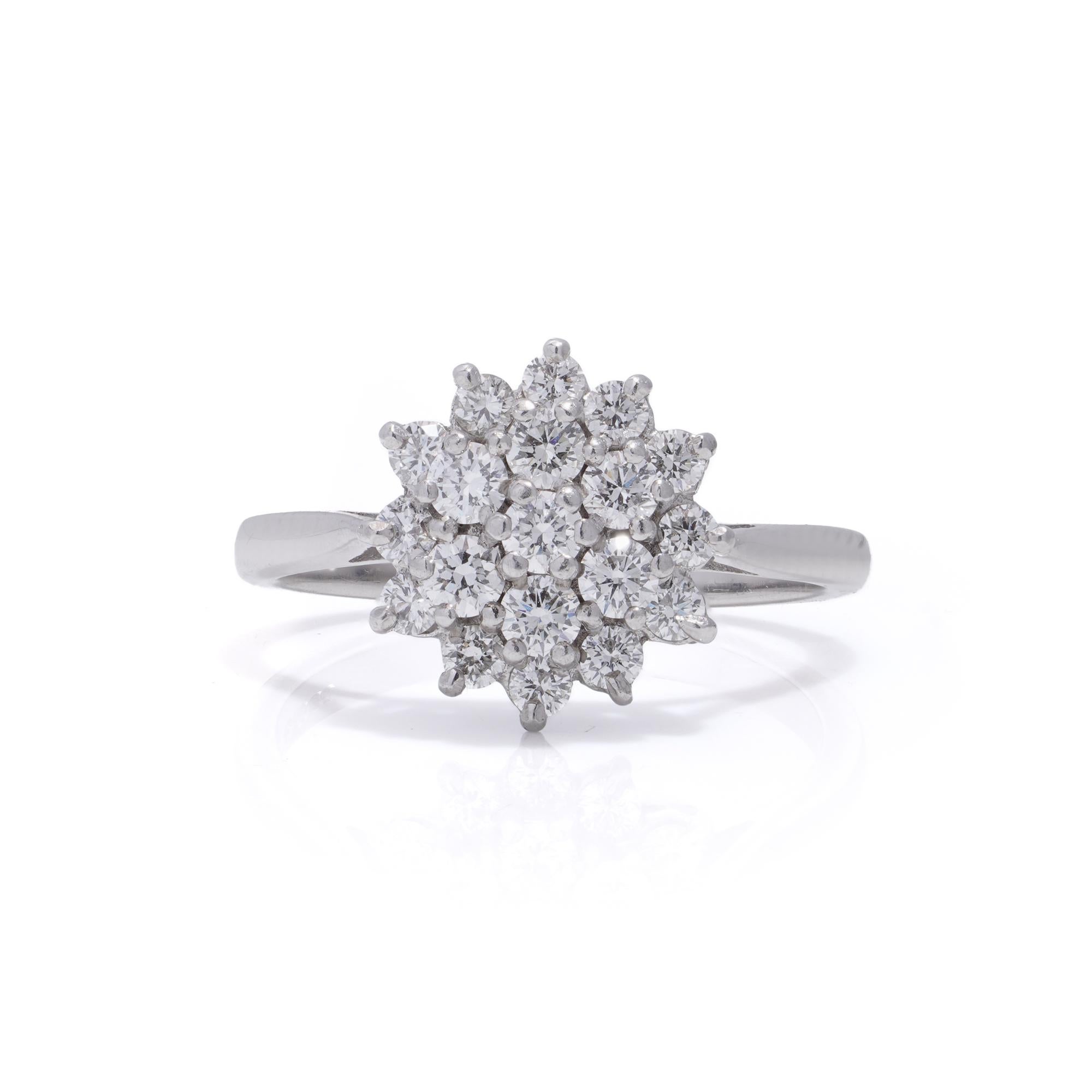 This exquisite Vintage ring boasts an 18kt yellow gold daisy flower design, adorned with dazzling diamonds. At its heart, a brilliant round cut diamond shines, encircled by eight smaller diamonds. The band is elegantly accented with two additional