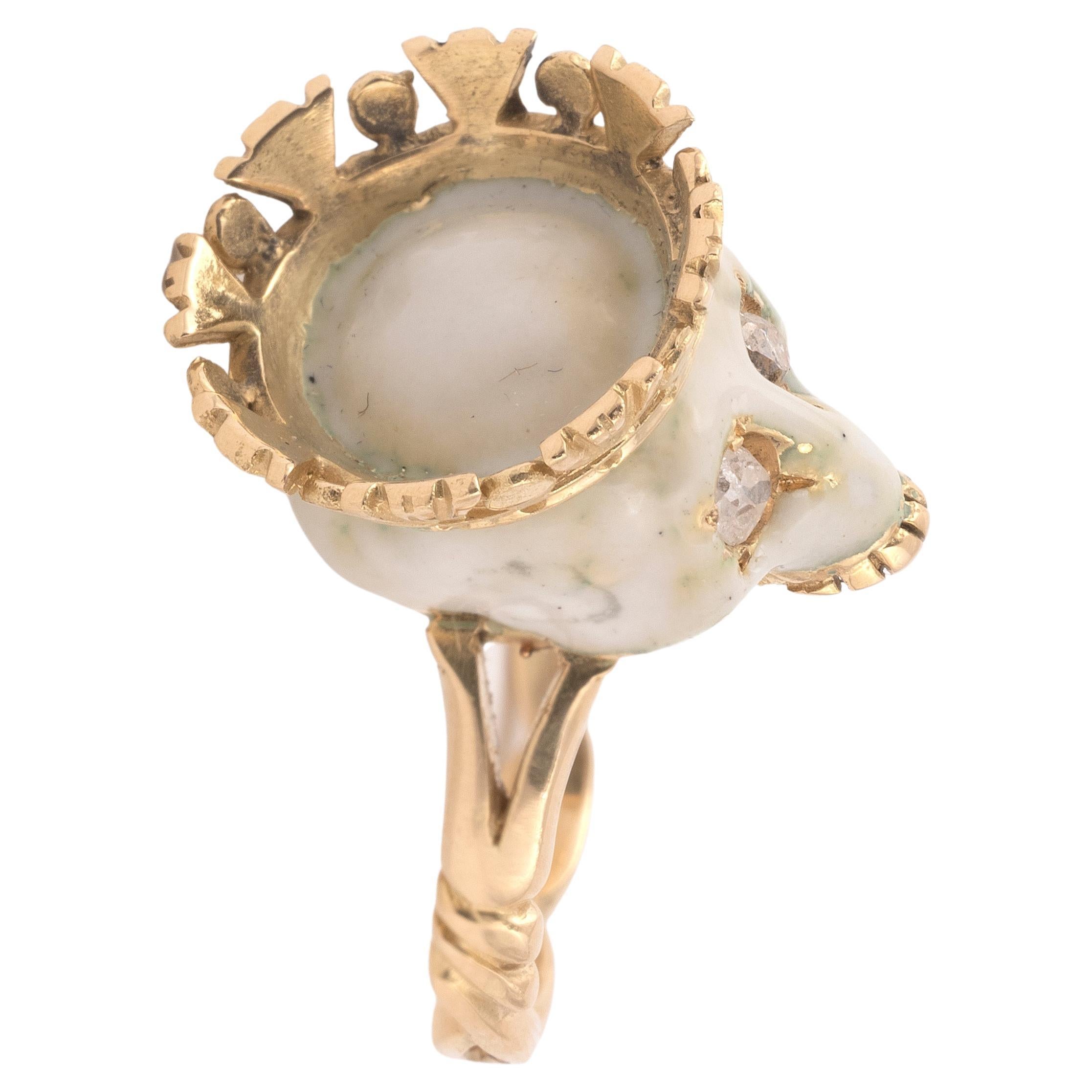 An enamel and diamond skull ring, the centre crowned skull and cream enamel with diamond-set eyes, to gold split shoulders and twisted designed shank, estimated total diamond weight 0.3cts, made by Gaetano Chiavetta
Size 7
Weight: 9,13gr