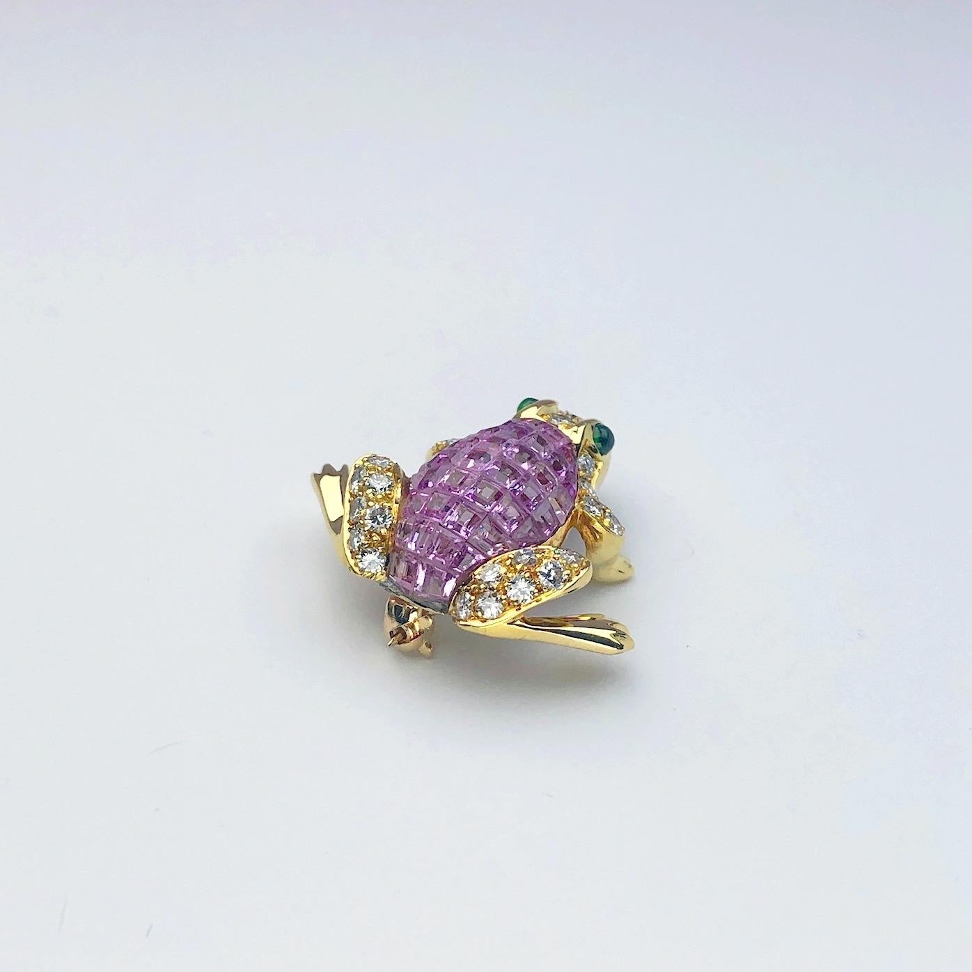 18 karat yellow gold frog brooch beautifully set with 6.12 carats of invisibly set  square pink sapphires and 0.70 carats of round diamonds. The eyes are cabochon emeralds. The frog measures 1