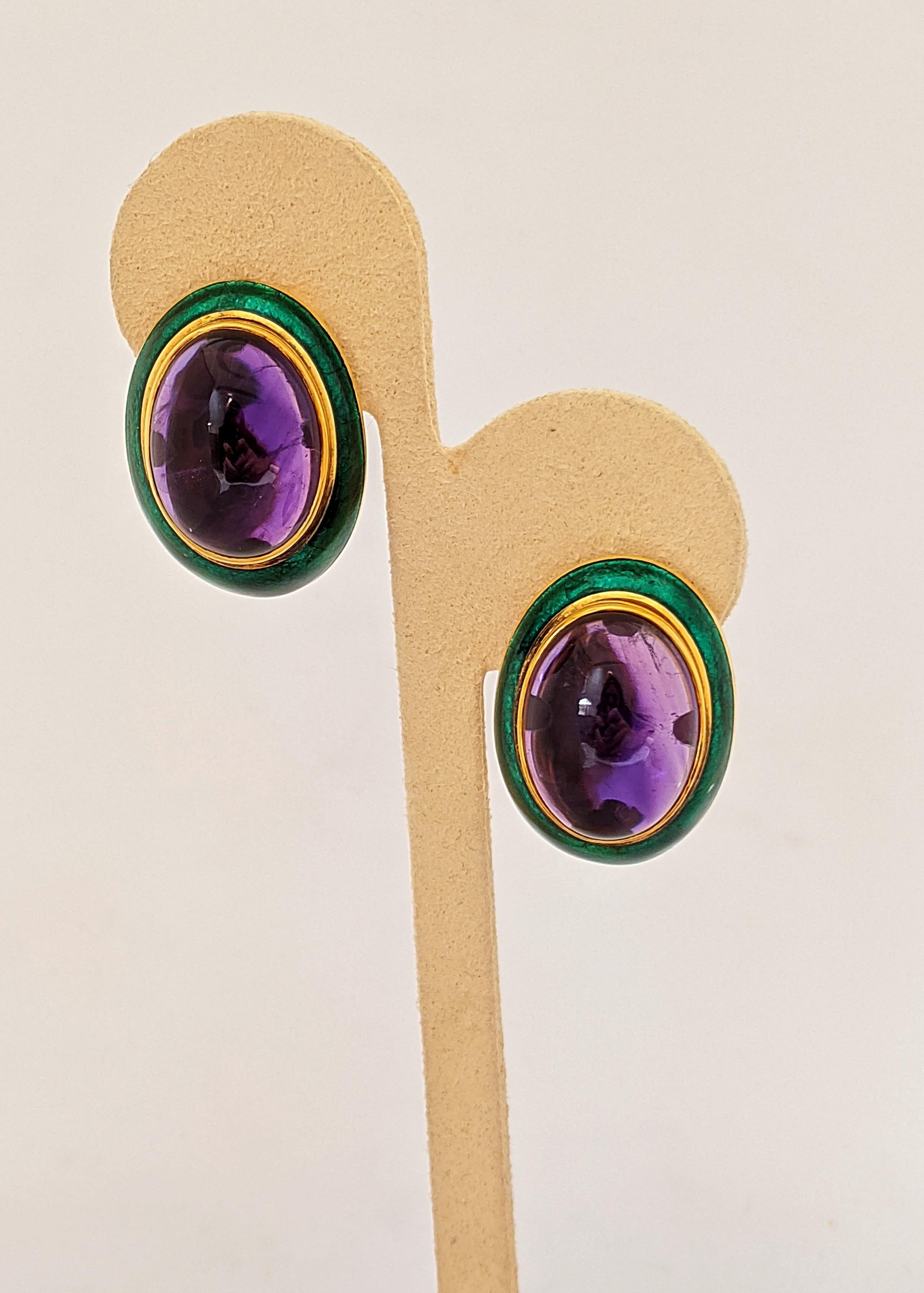 A striking combination of colors. These 18 karat yellow gold earrings feature large oval cabochon Amethyst centers. The center stones are set in a gold bezel surrounded by a vibrant green enamel setting. The earrings measure 1 1/8