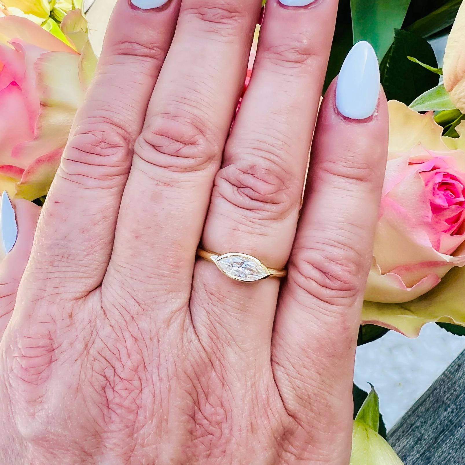 A modern take on a classic design. This unique 18 karat yellow gold engagement ring features a natural marquise cut diamond expertly bezel set in its east-west position with an open basket design allowing for maximum light to enter and deliver