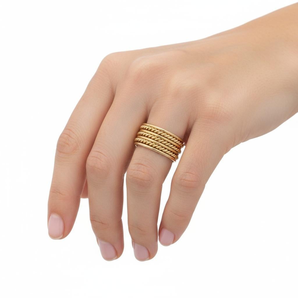 Questo elegante anello a fascia multipla è sapientemente realizzato in oro giallo 18 carati e presenta un'abile combinazione di motivi intrecciati e semplici che creano interesse visivo e consistenza. L'armoniosa interazione tra le fasce lucide e