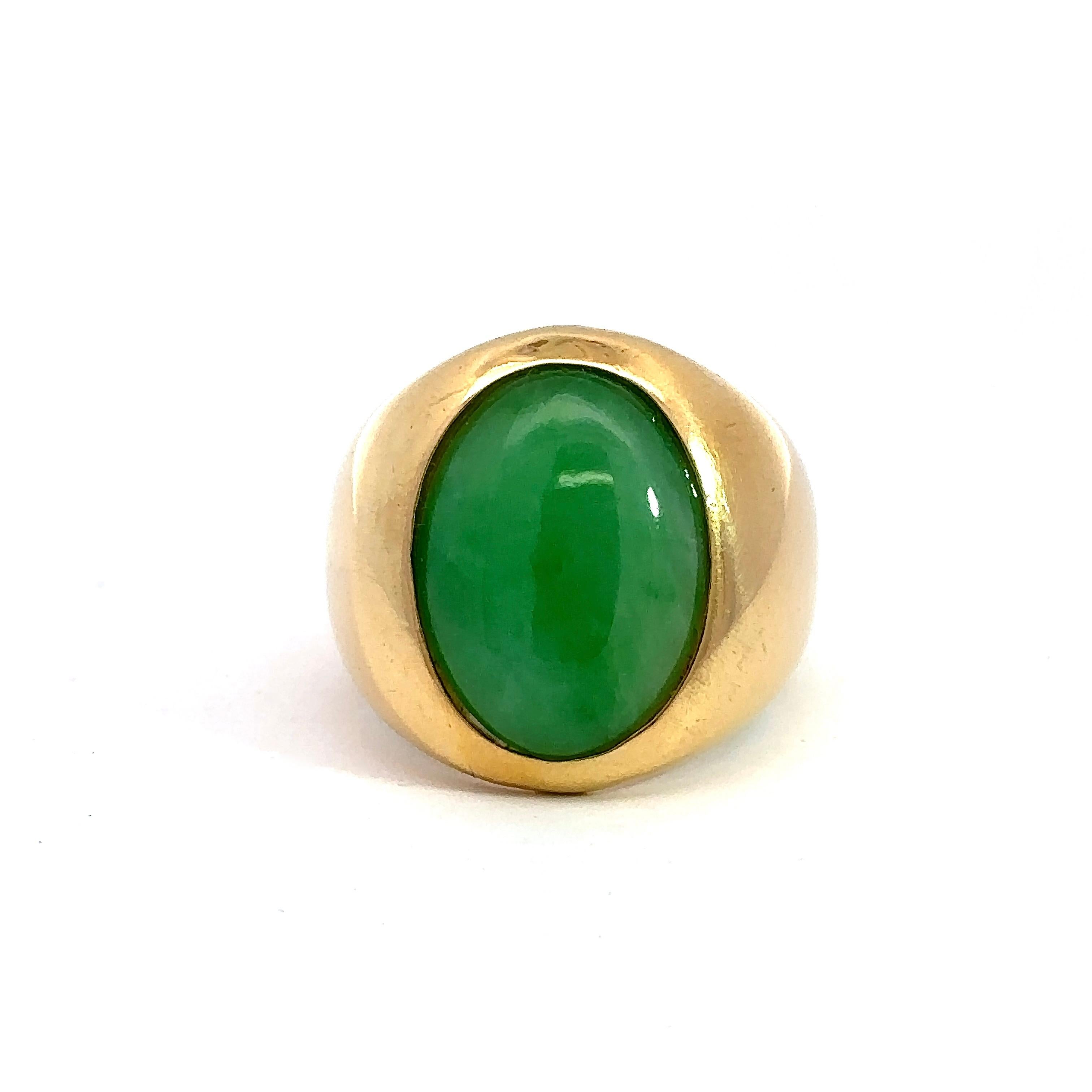 Cette bague de chevalière en jade cabochon ovale est réalisée en or jaune 18KT et date des années 1970. Le jade vert ovale, serti en biseau, mesure environ 16 mm x 12 mm et la tige se rétrécit jusqu'à 6 mm. La bague est de taille 6,5 et peut être