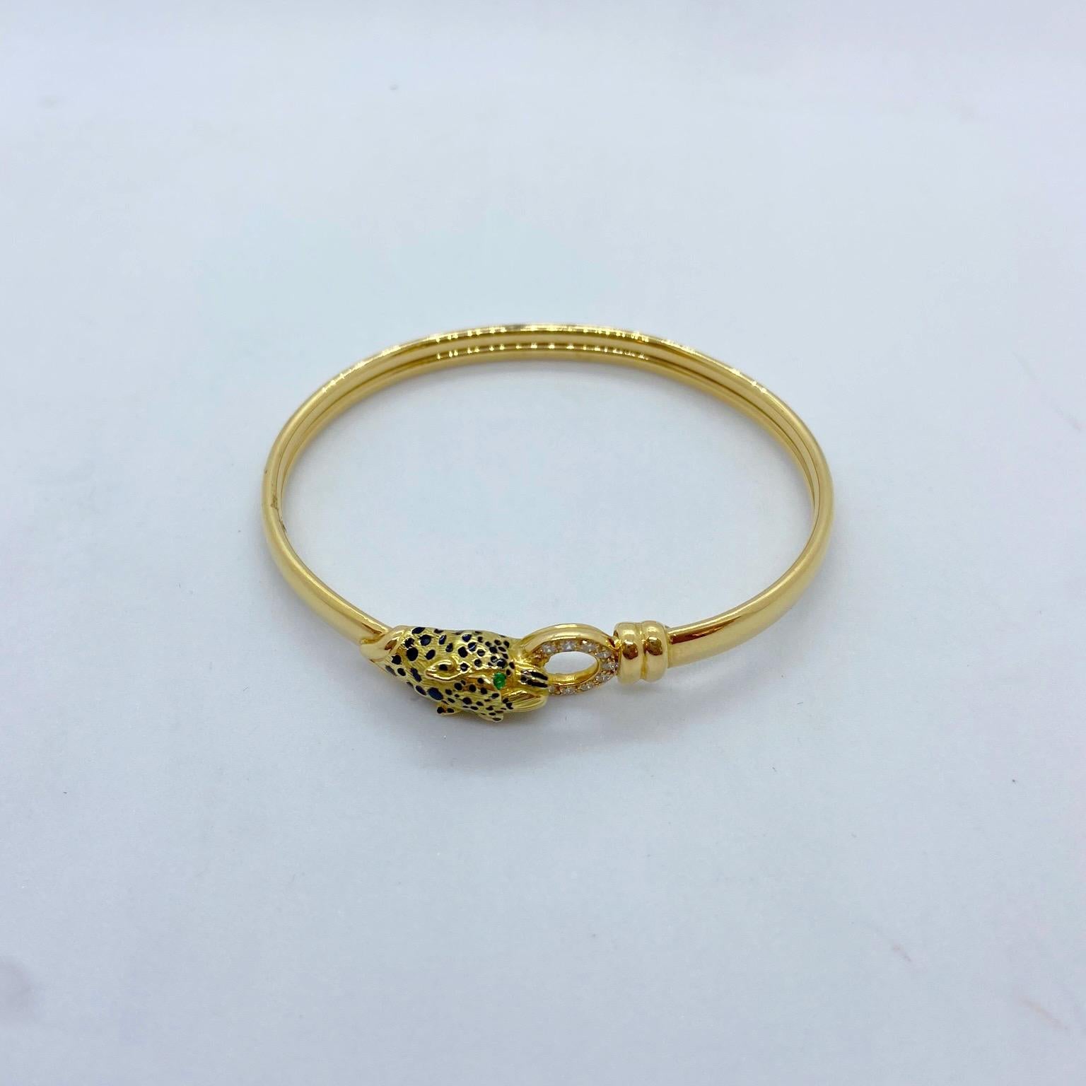 This 18 karat yellow gold bangle is designed with a Panthers head, Emerald eyes and Black enamel spots. His mouth holds a ring set with round brilliant Diamonds. The bracelet unlocks at the top .The inside measurement is 2.5