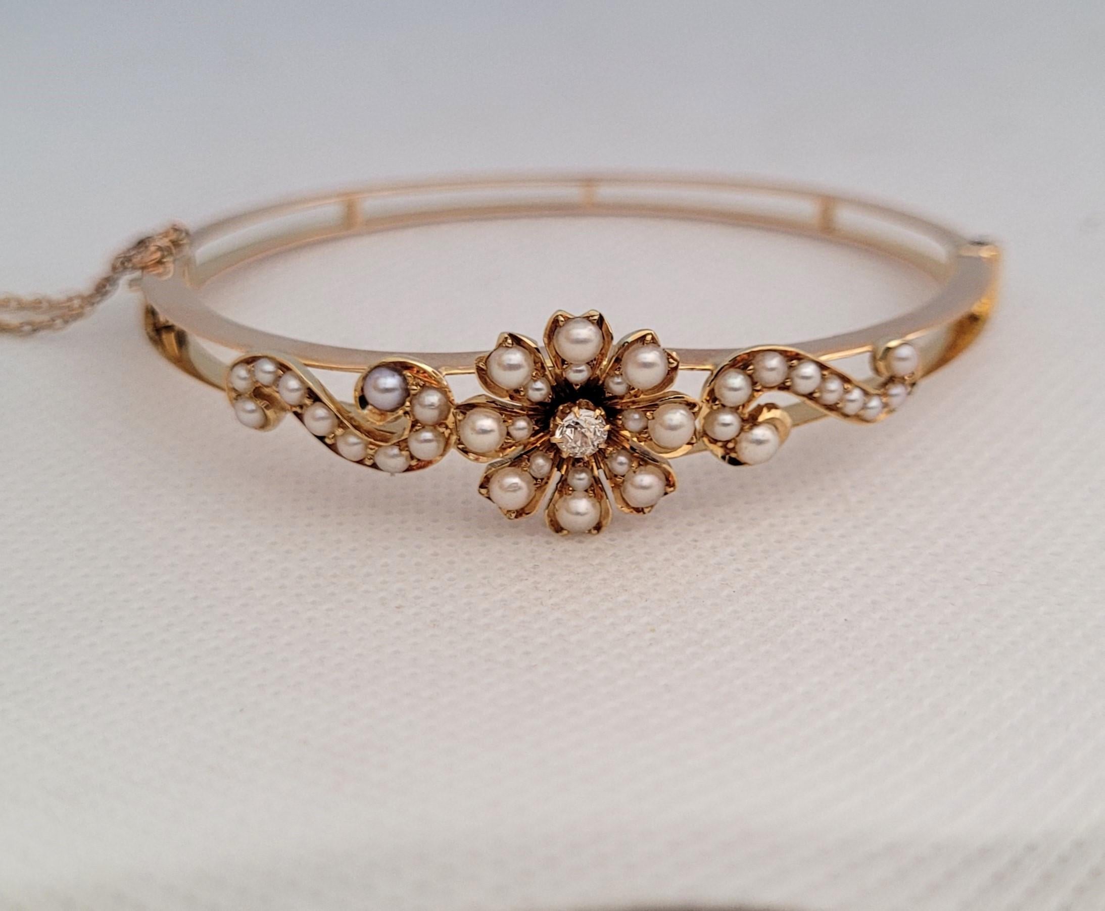 This is an 18kt yellow gold vintage bracelet with 36 white pearls and one 2.9mm old mine-cut diamond. The hinged bracelet features a beautiful floral scroll design and is secured with a safety chain. The outer diameter of the bracelet is 56mm x