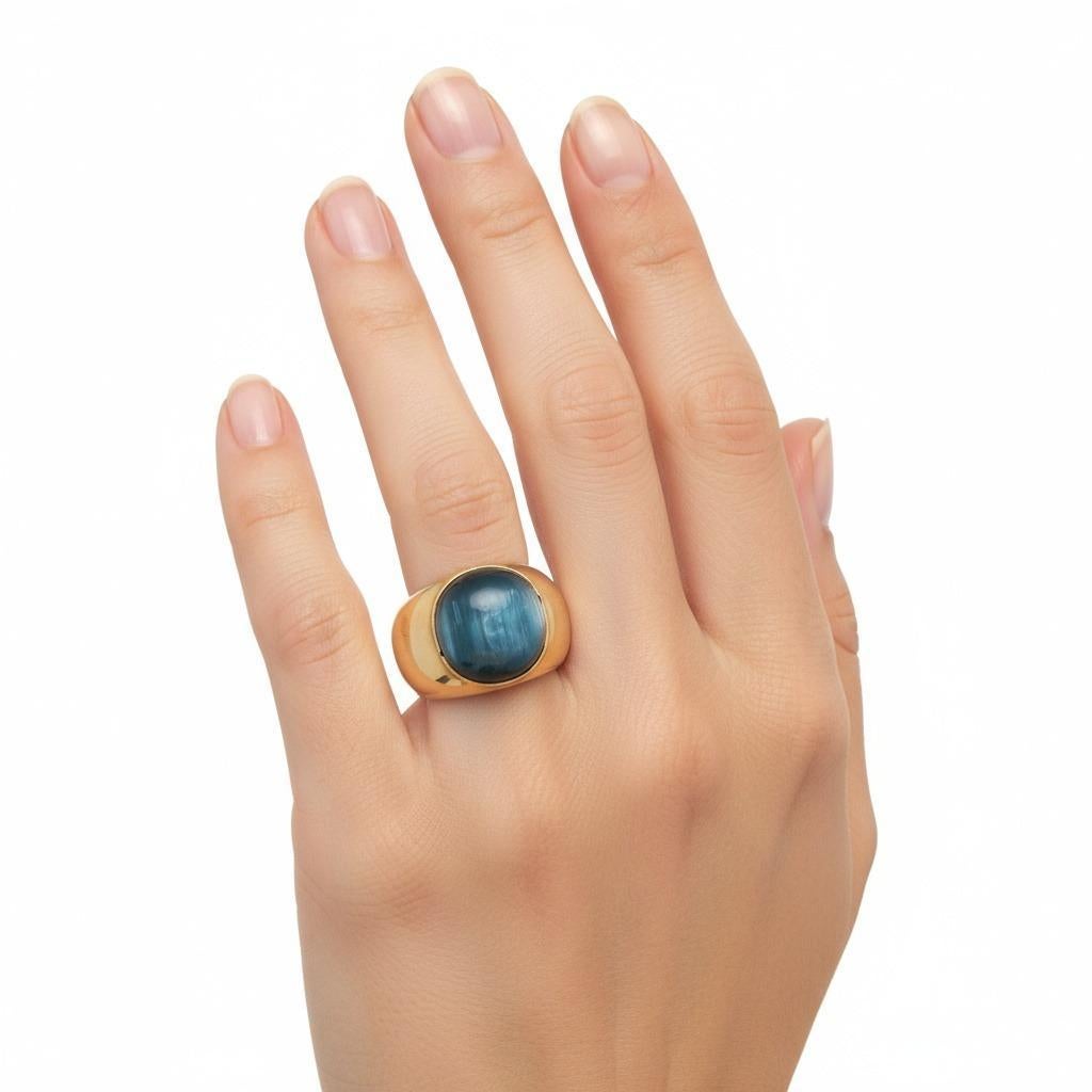 Cette magnifique bague large est réalisée en or jaune 18 carats et sertie d'un saphir bleu œil de chat cabochon d'environ 11,75 carats. La pierre précieuse affiche un effet chatoyant hypnotisant, avec une bande lumineuse qui se déplace gracieusement