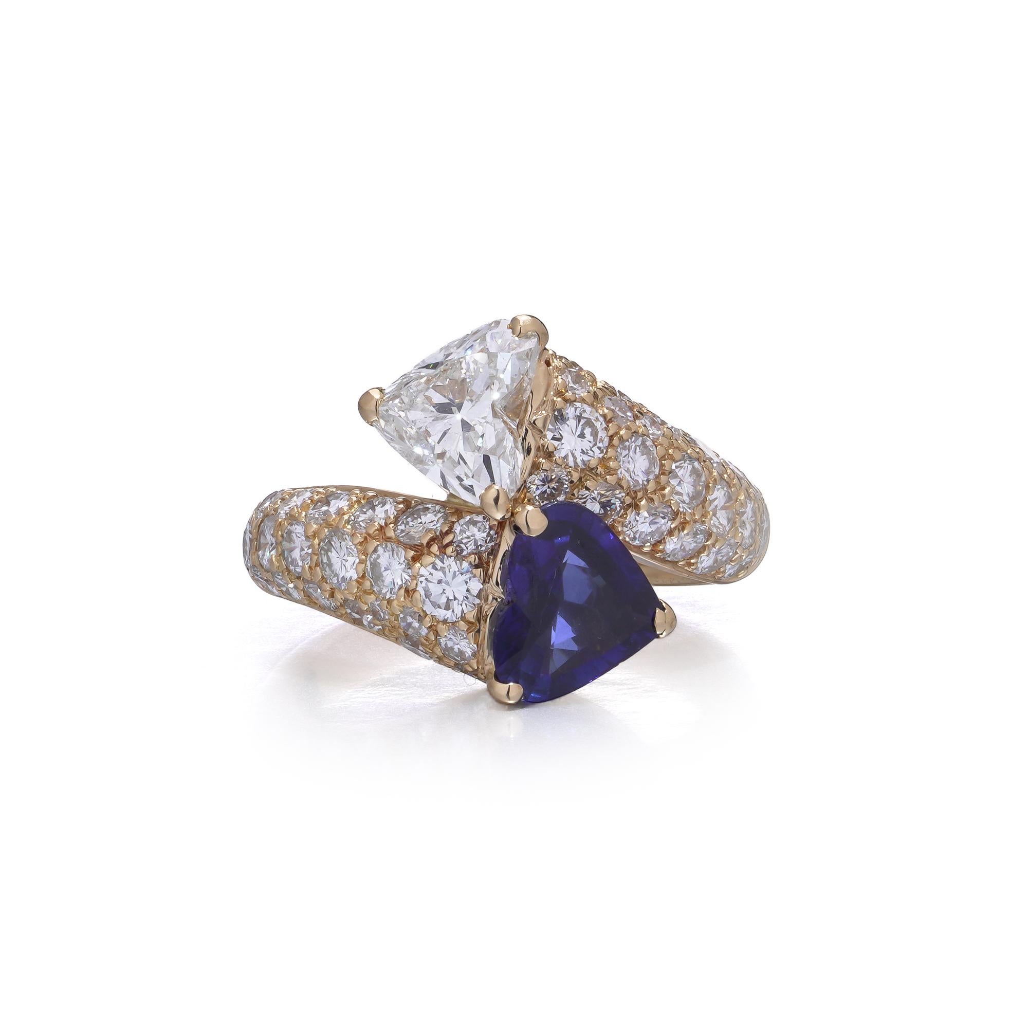Élégante bague croisée en or jaune 18kt sertie d'un saphir en forme de cœur et d'un diamant en forme de cœur, accentués par des diamants taille brillant pavés. Le design/One symbolise l'unité et le romantisme, ce qui en fait un bijou