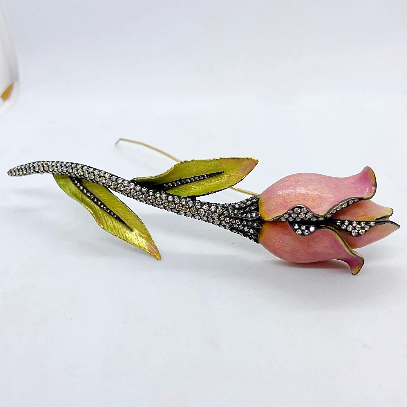 This 18 karat yellow gold rose brooch is designed with opalescent pink enamel for the flower and greenish yellow enamel for the leaves. The stem is set with round brilliant diamonds set in a blackened sterling silver. The leaves and petals are also
