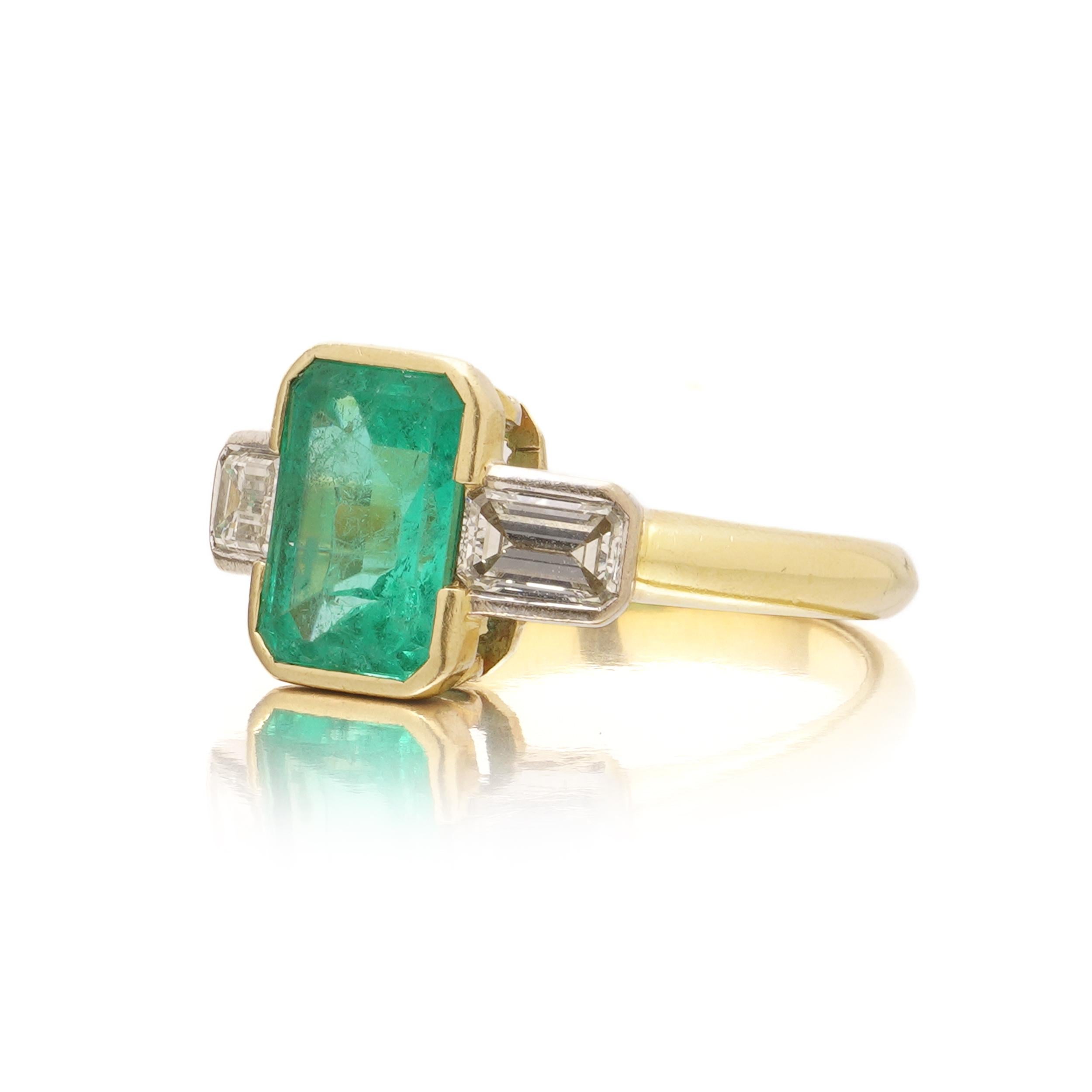 Ein eleganter Dreisteinring aus 18 Karat Gelbgold mit einem leuchtenden Smaragd im Stufenschliff in der Mitte, flankiert von zwei Diamanten im Baguetteschliff. Der Smaragd ist sicher in der Lünette gefasst und zeigt eine lebhafte grüne Farbe mit