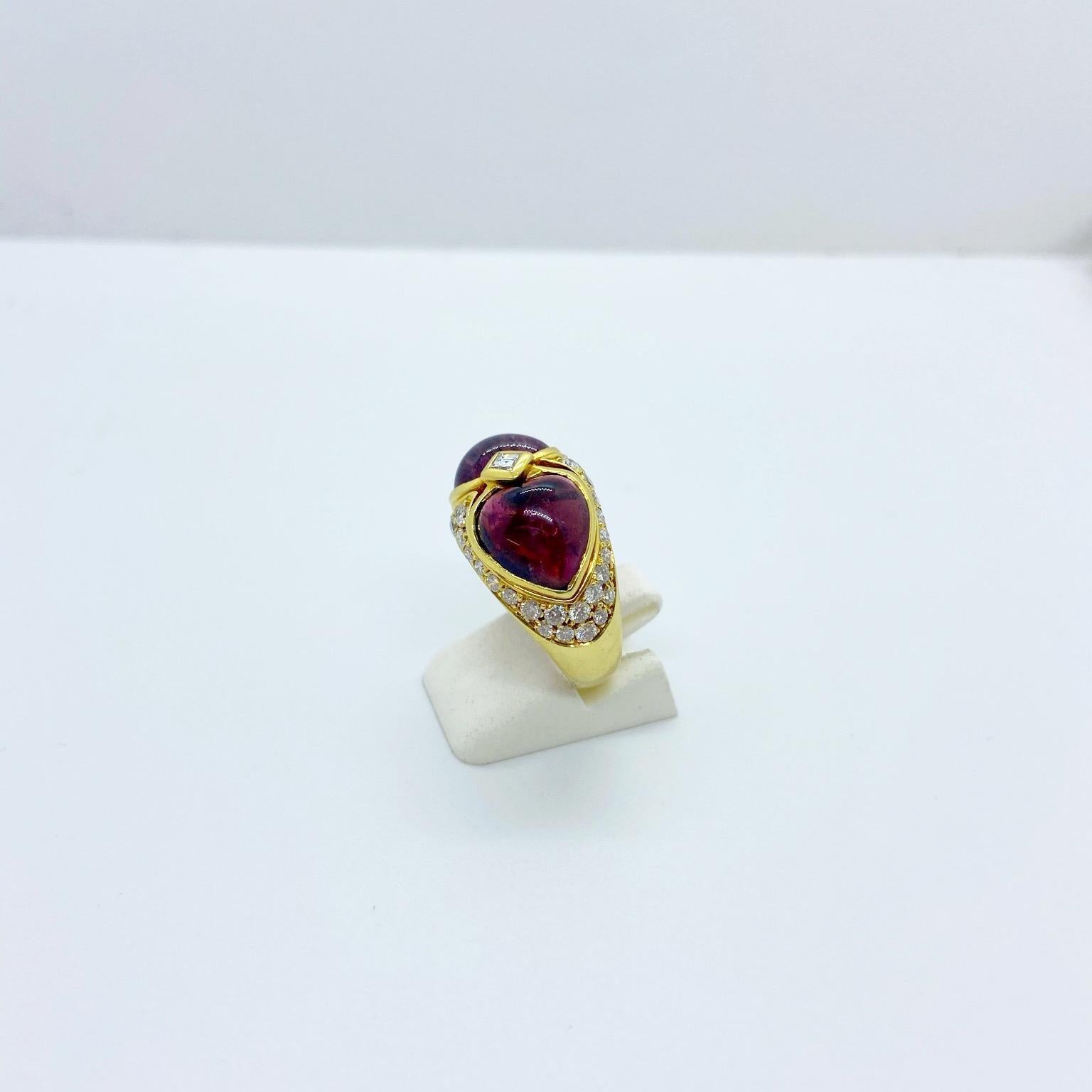 Two cabochon rubelite  hearts are the centerpiece of this 18 karat yellow gold ring. The hearts are joined in the center by a bezel set square cut diamond and accented all around with pave round brilliant diamonds.
Rubellite weight 8.25